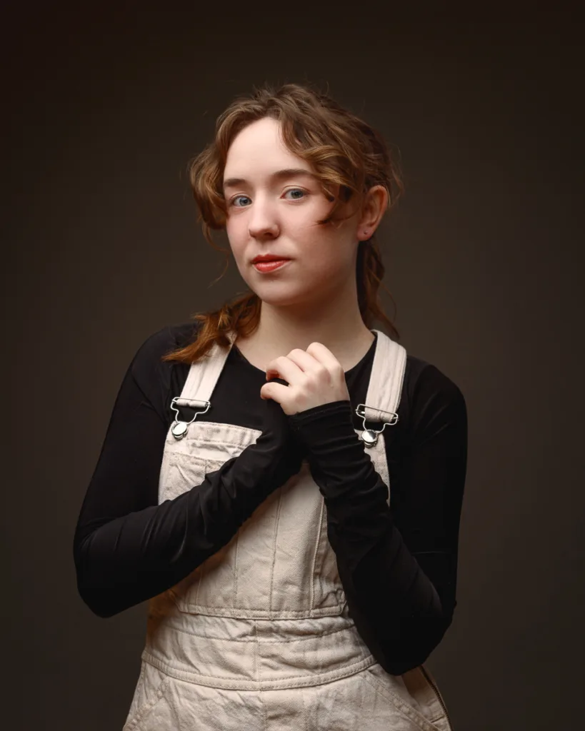 Person wearing dungarees posing against dark background
