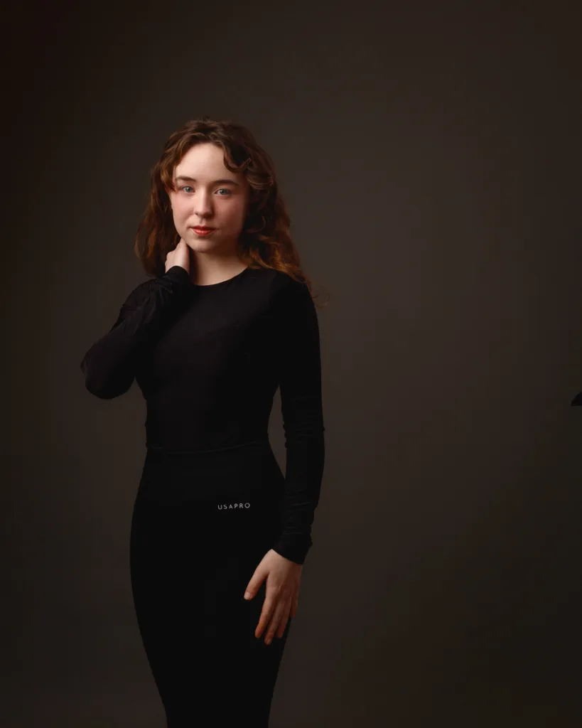 Person posing in black outfit against dark background
