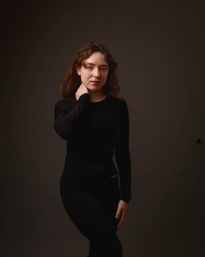 Person posing in dark clothing against plain background