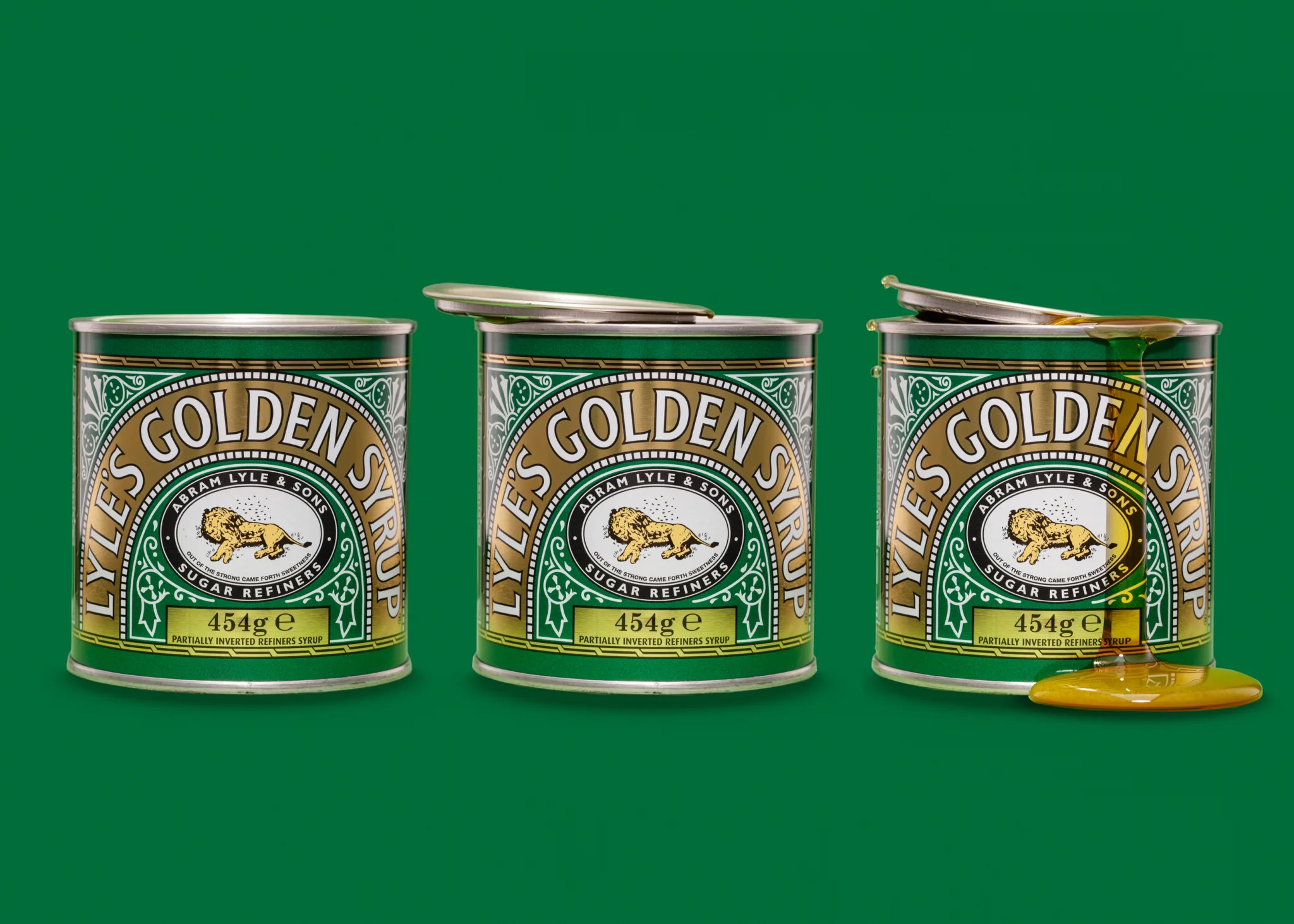 Three tins of Lyle's Golden Syrup on green background