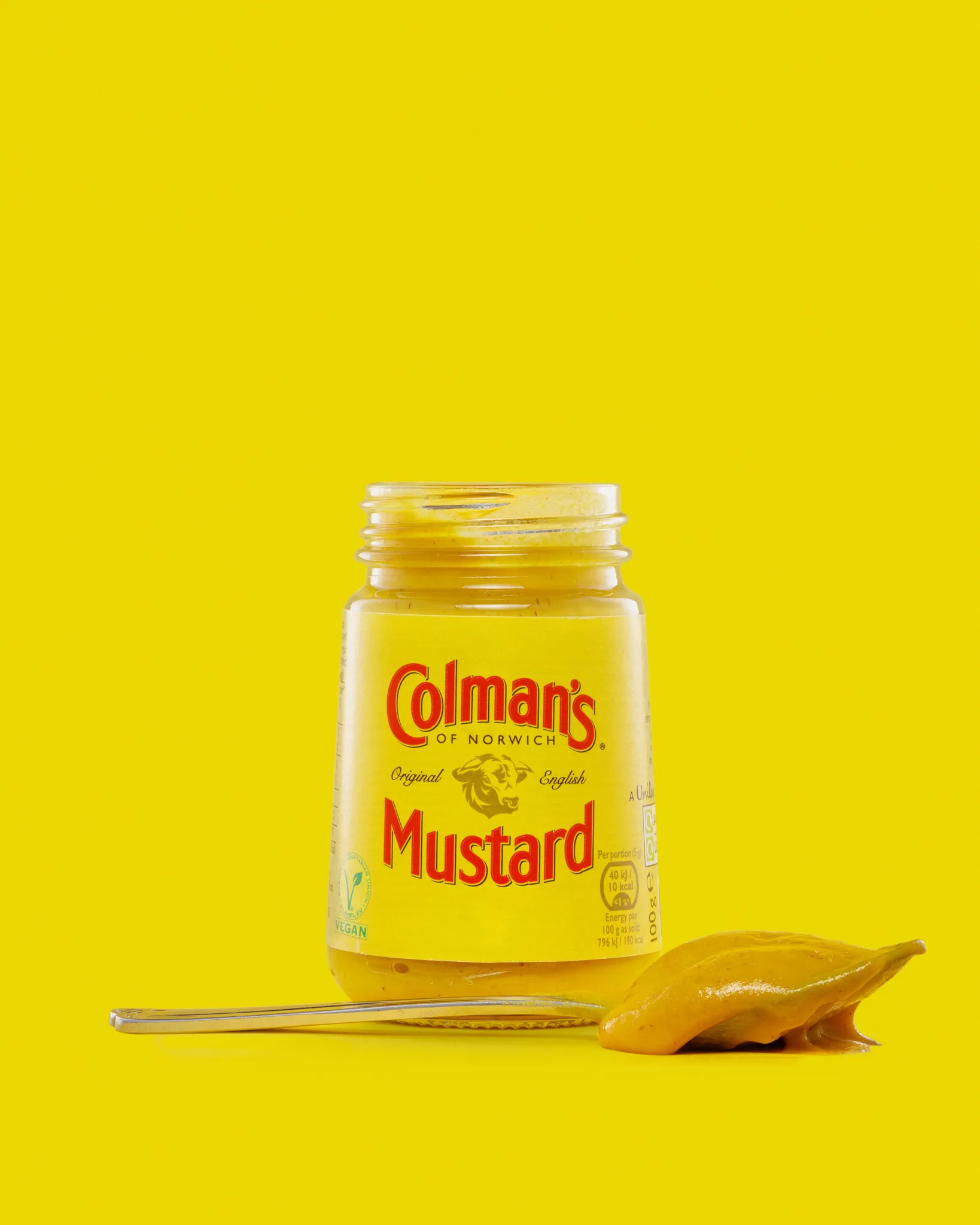 Jar of Colman's mustard with spoon on yellow background