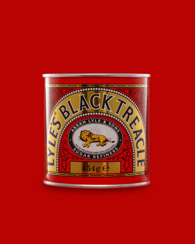 Product photograph of a tin of Lyle's Black Treacle on a red background