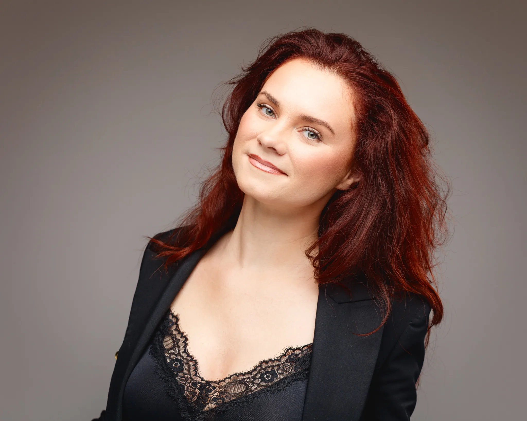 Smiling woman with red hair in black blazer.