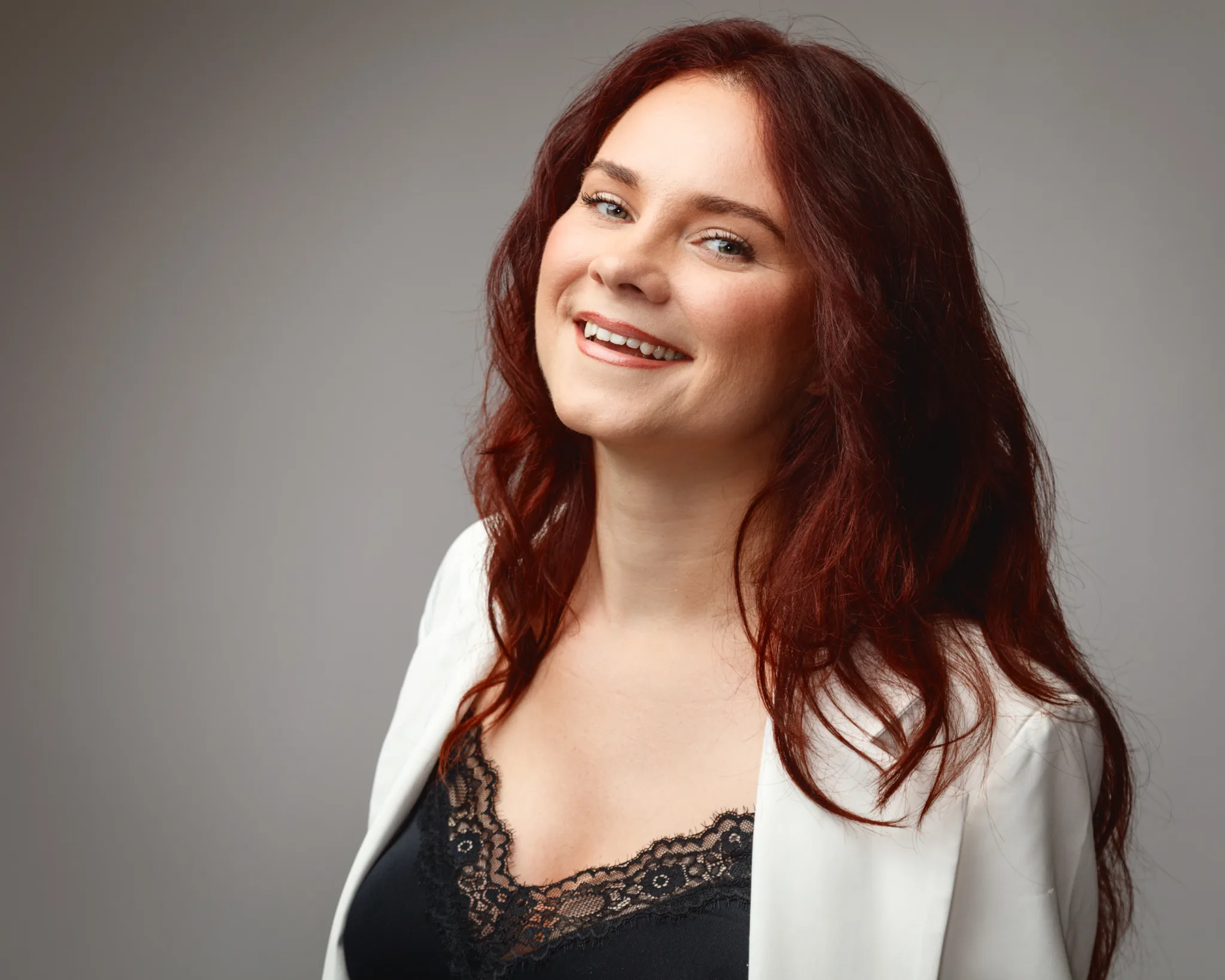 Smiling woman with long red hair and lace top.