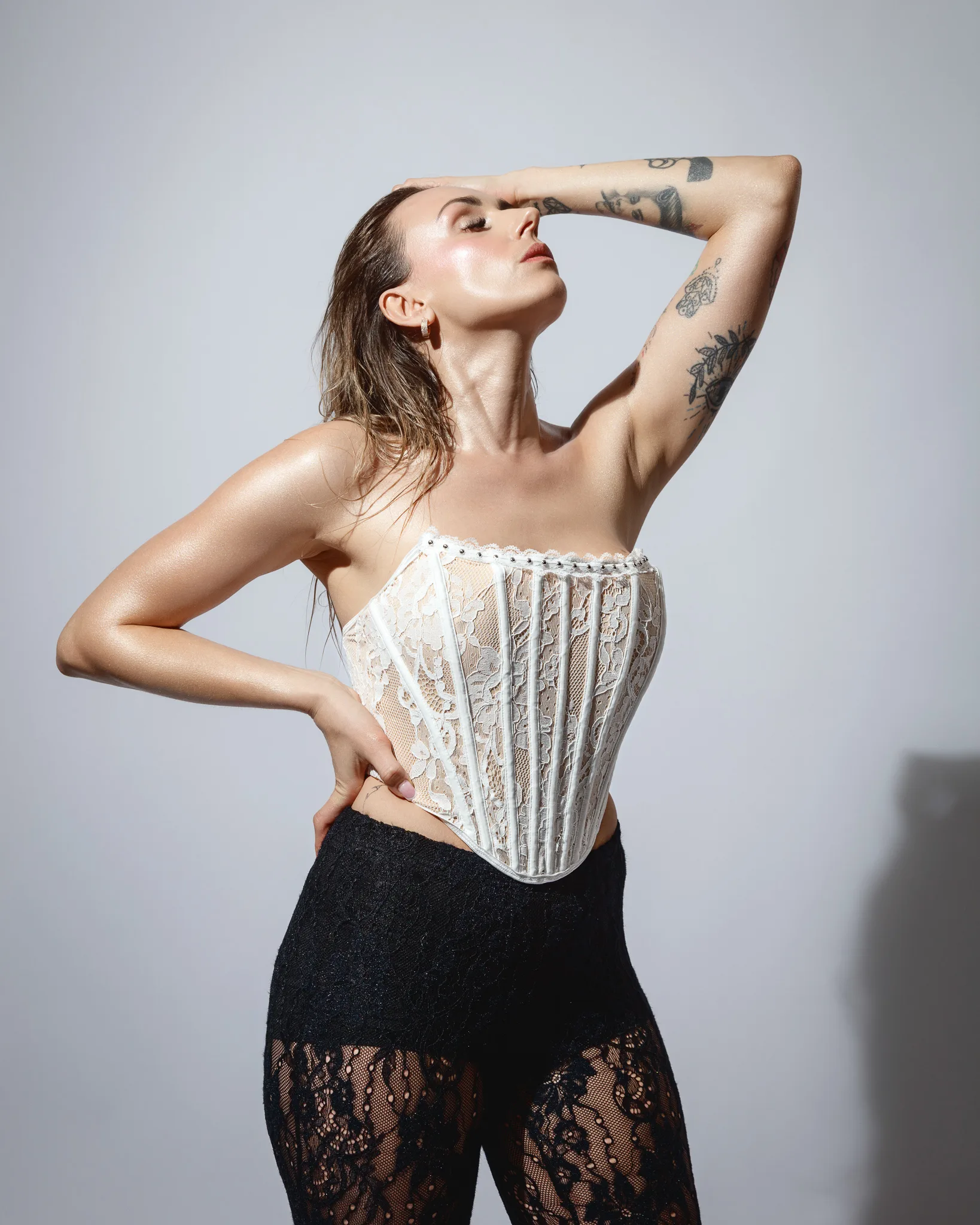 Person in lace corset and trousers, tattoos visible.