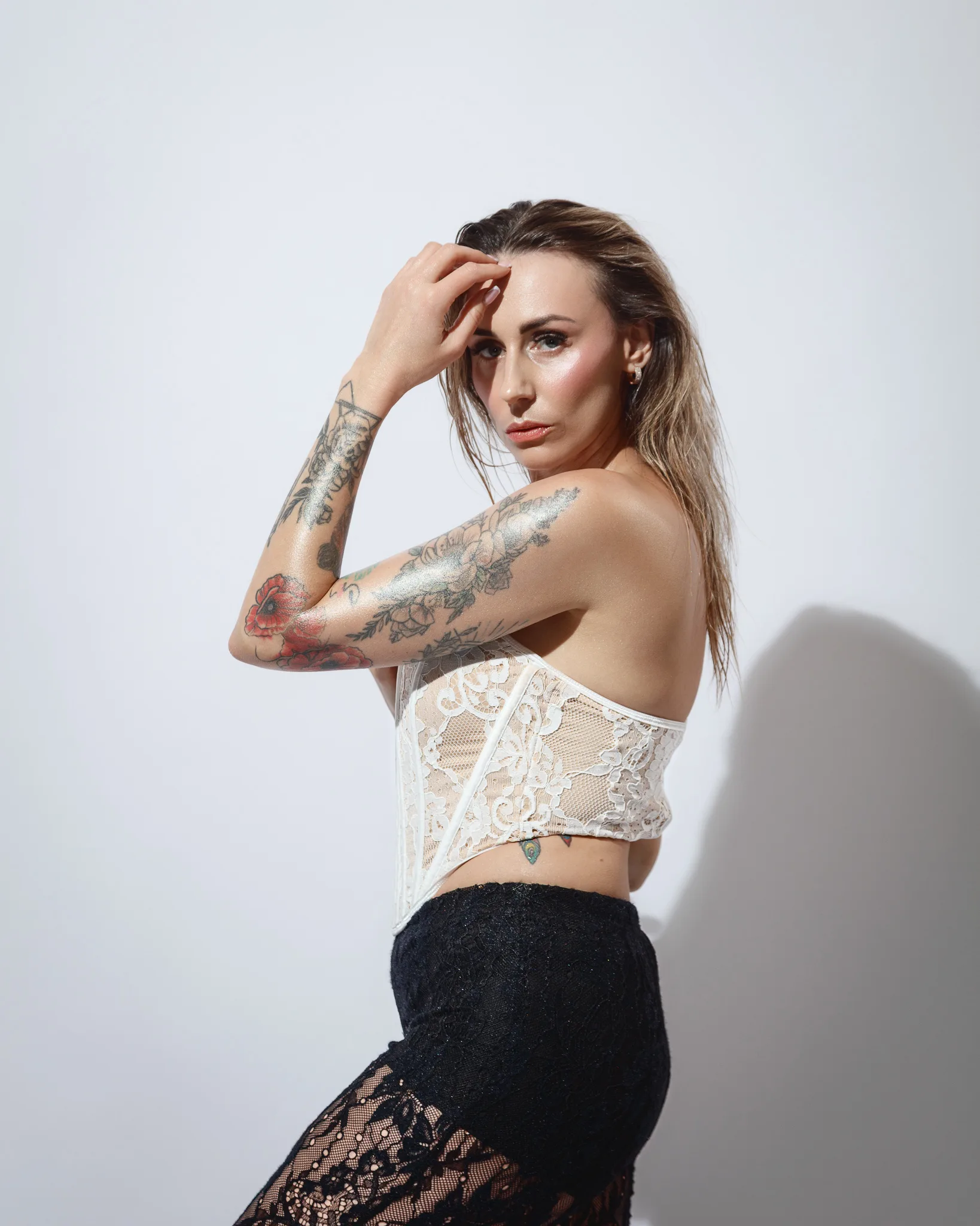 Tattooed woman in lace top poses elegantly.