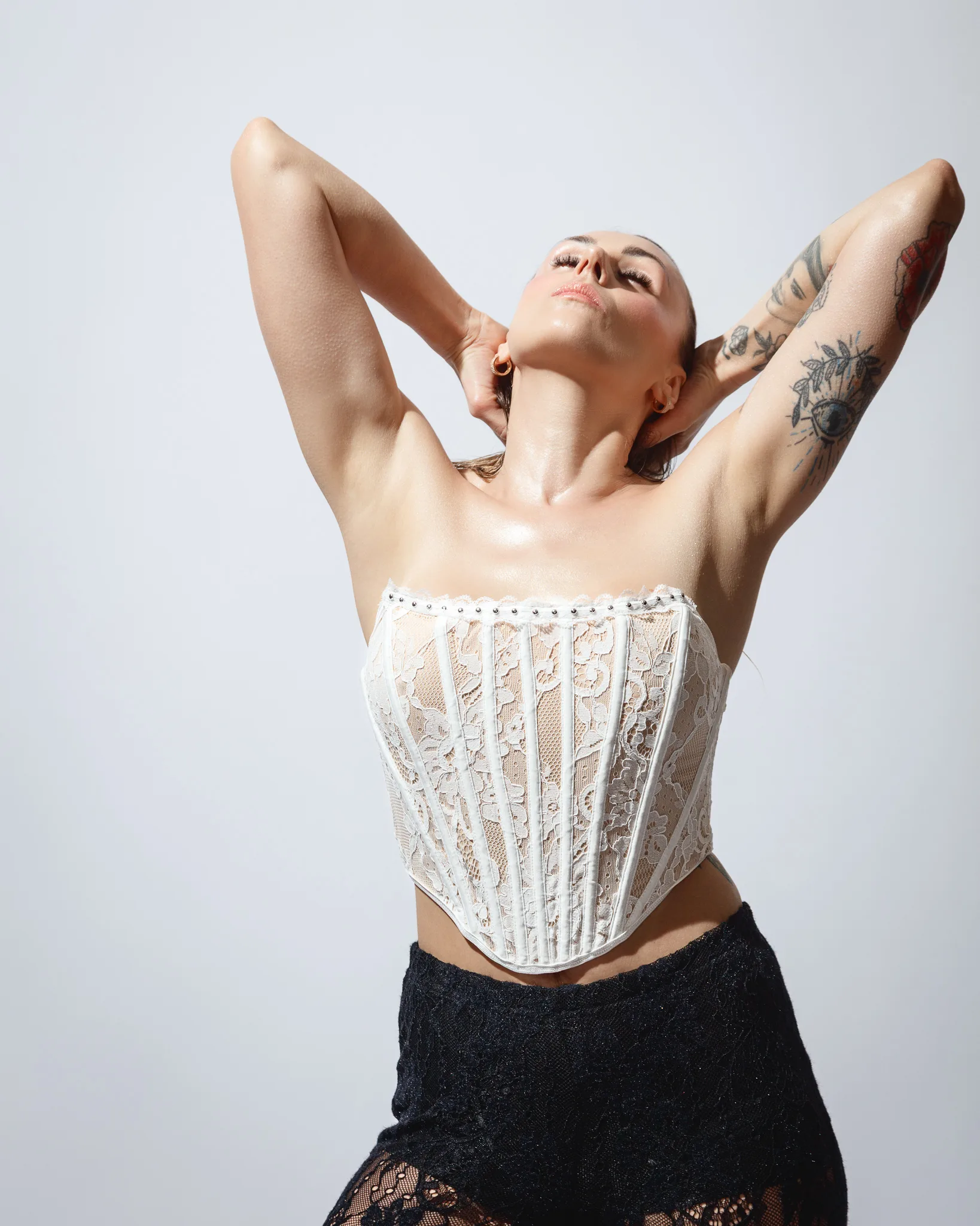 Person posing in lace corset and tattooed arms