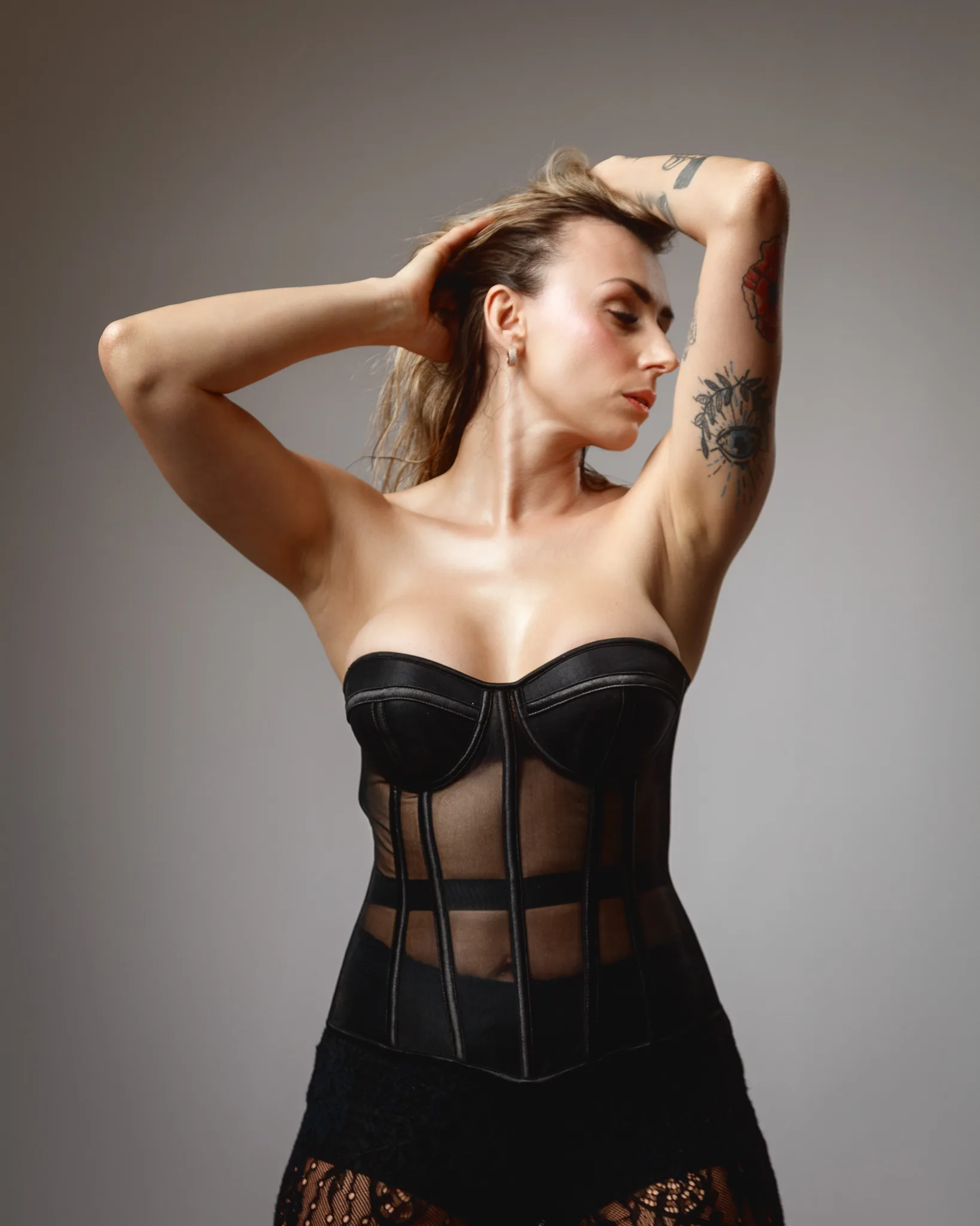 Model in black corset with tattoos posing elegantly.