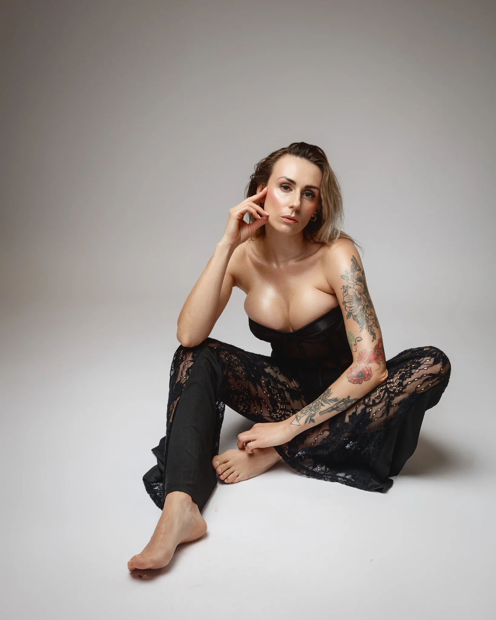 Tattooed woman in black lace outfit sitting pose.