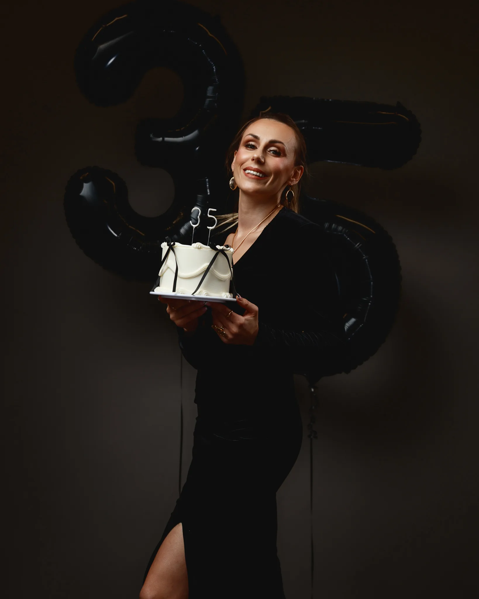 Woman holding cake with 35 balloons behind.
