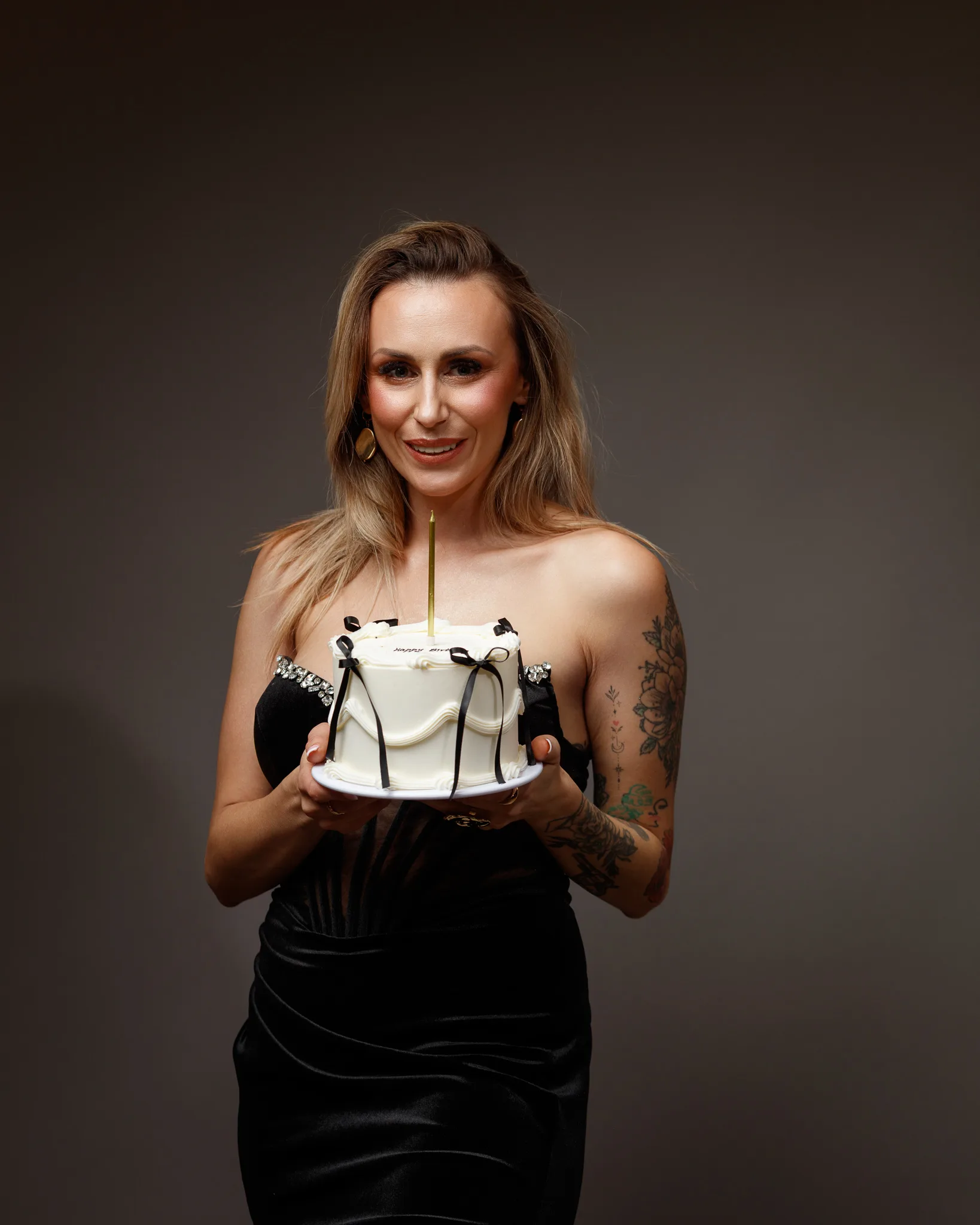 Woman in black dress holding decorated cake.