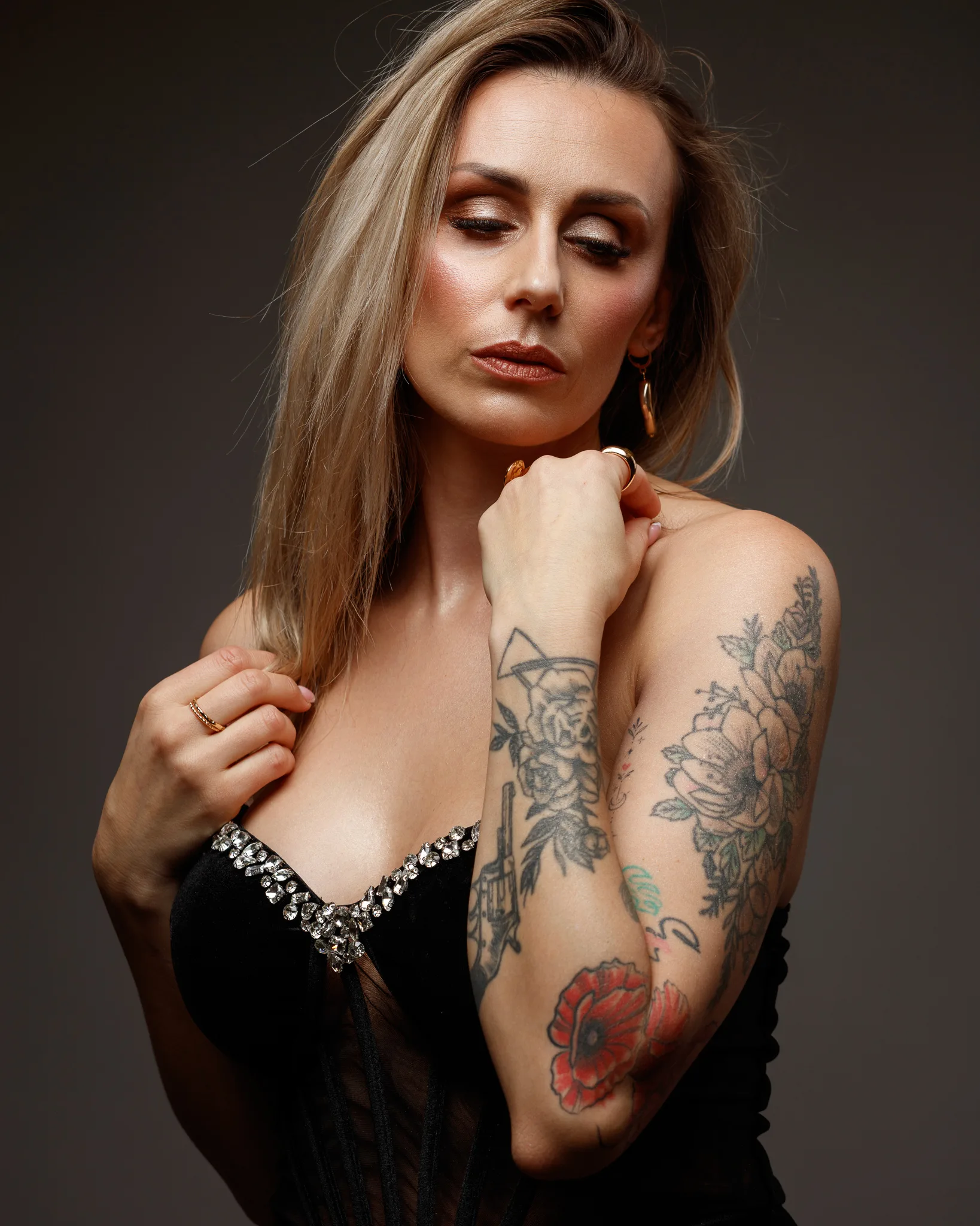 Woman with tattoos, glamorous dress, thoughtful pose.