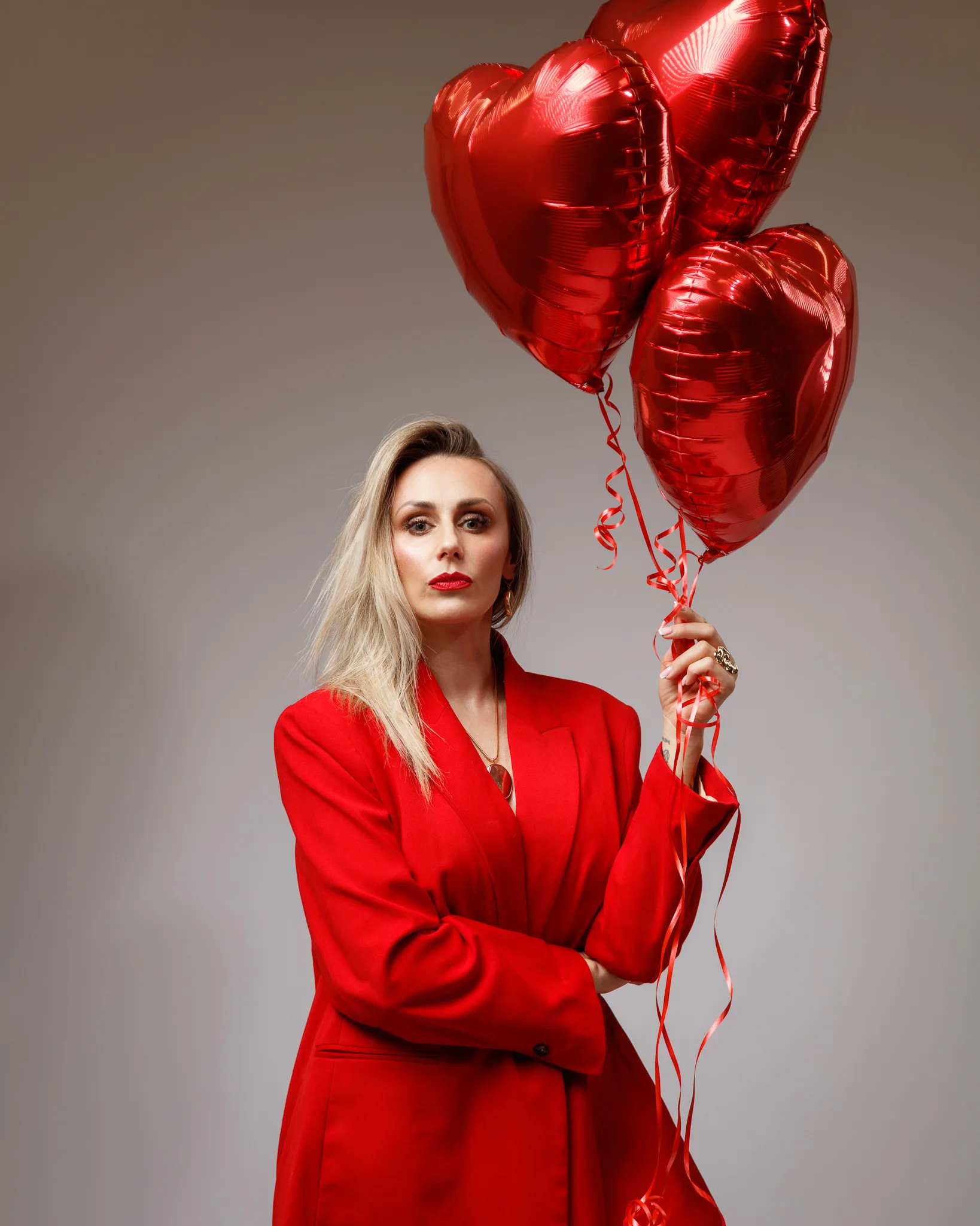 Woman in red suit holding heart-shaped balloons.