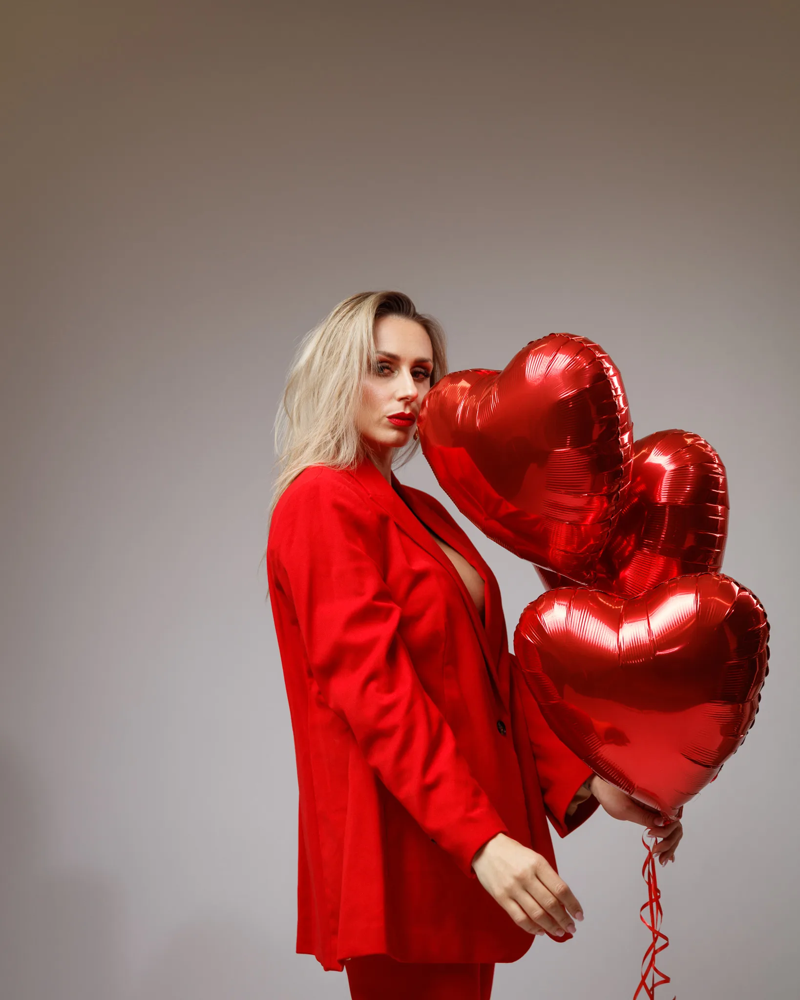 Person holding red heart-shaped balloons in red outfit.