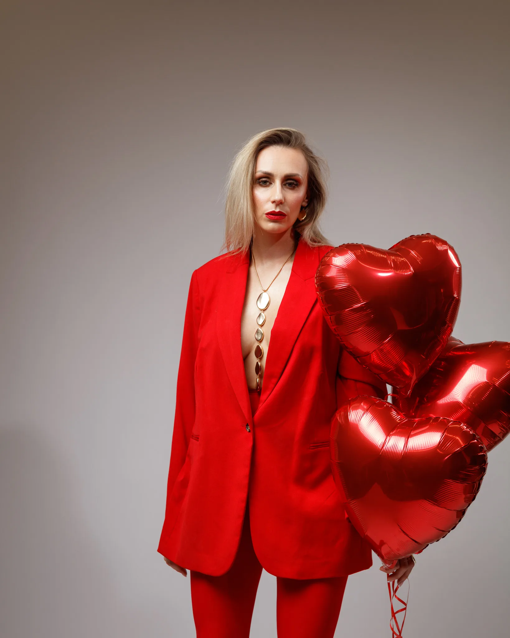 Person in red suit holding heart-shaped balloons.