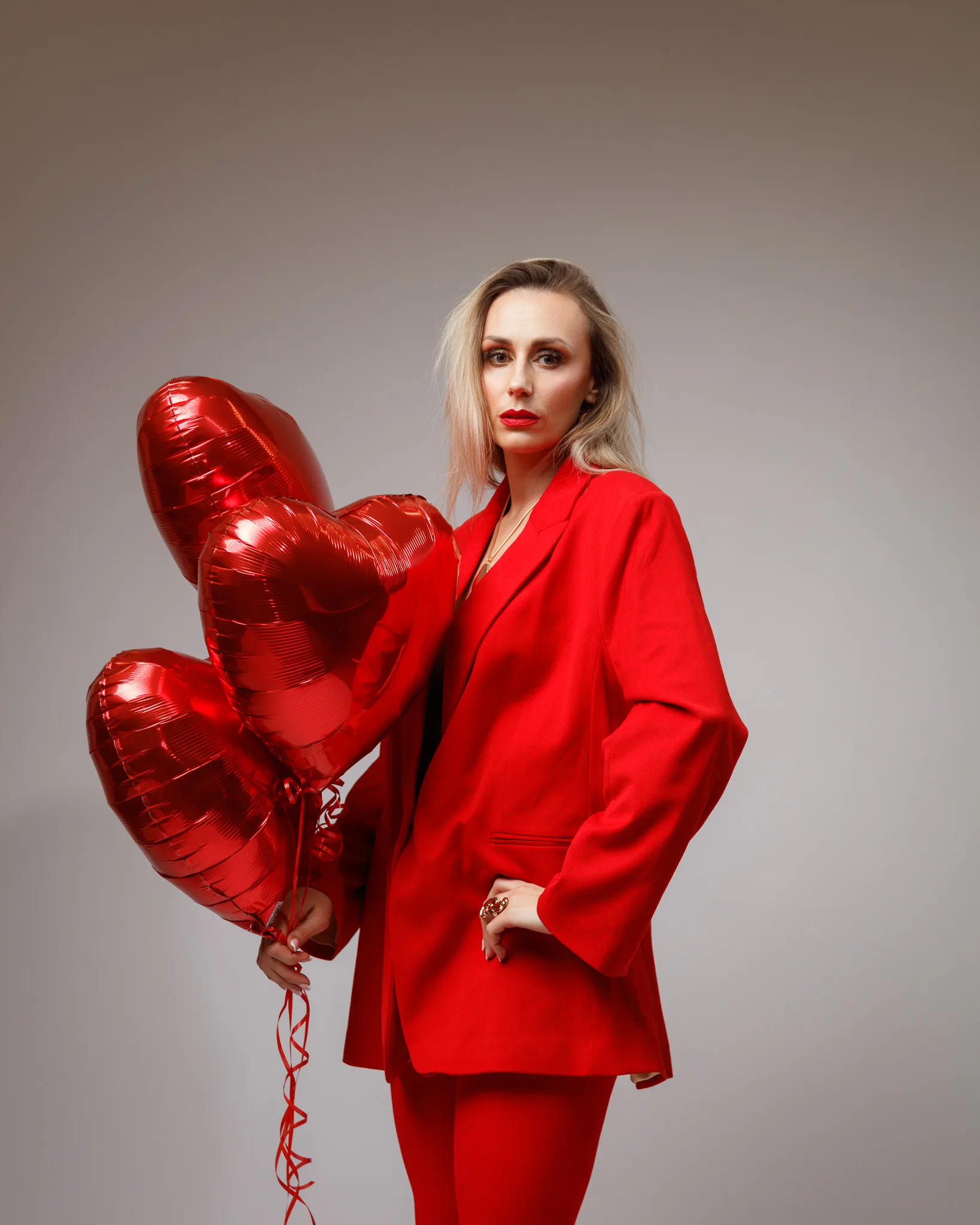 Woman in red suit holding heart balloons.