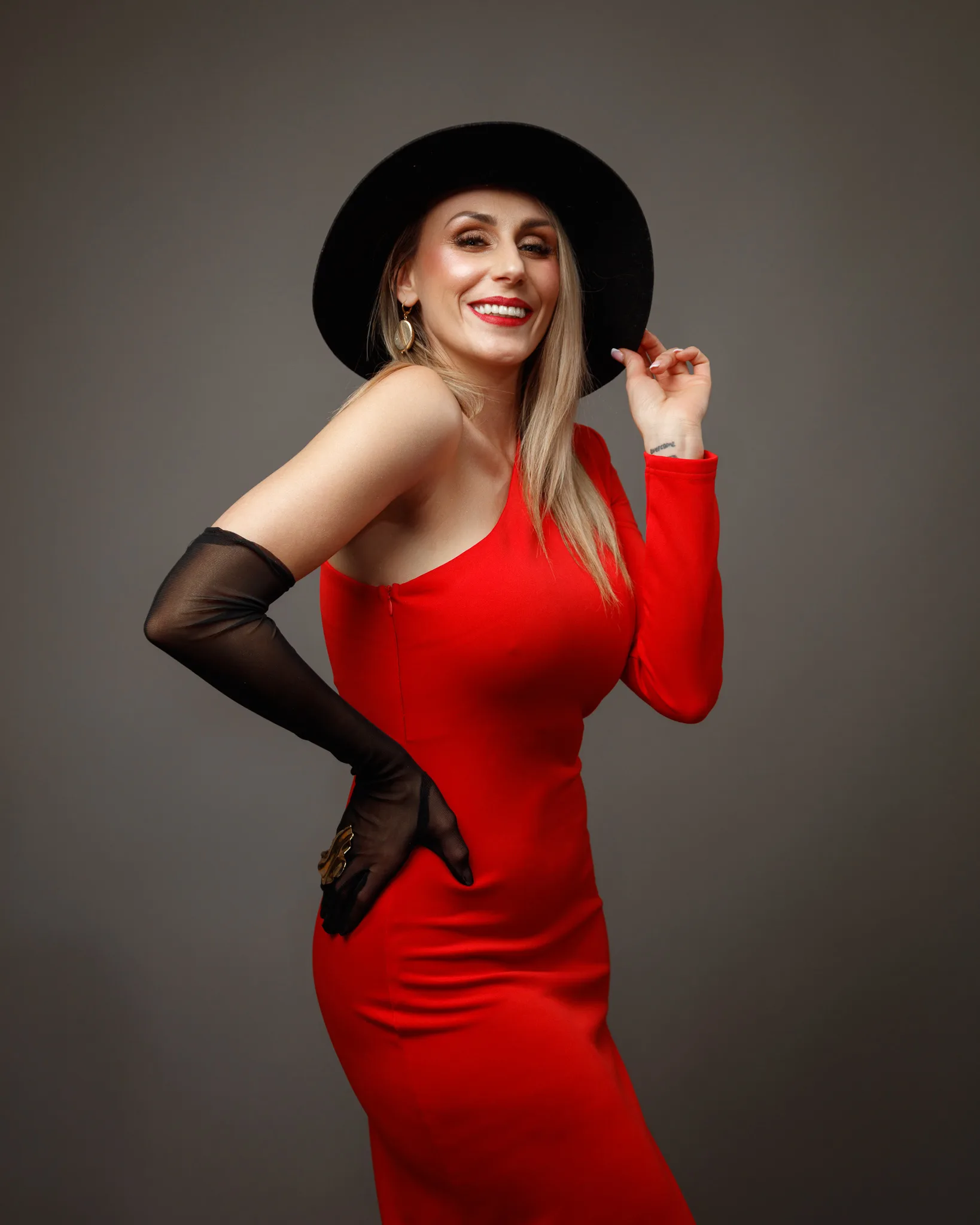 Smiling woman in red dress and black hat.