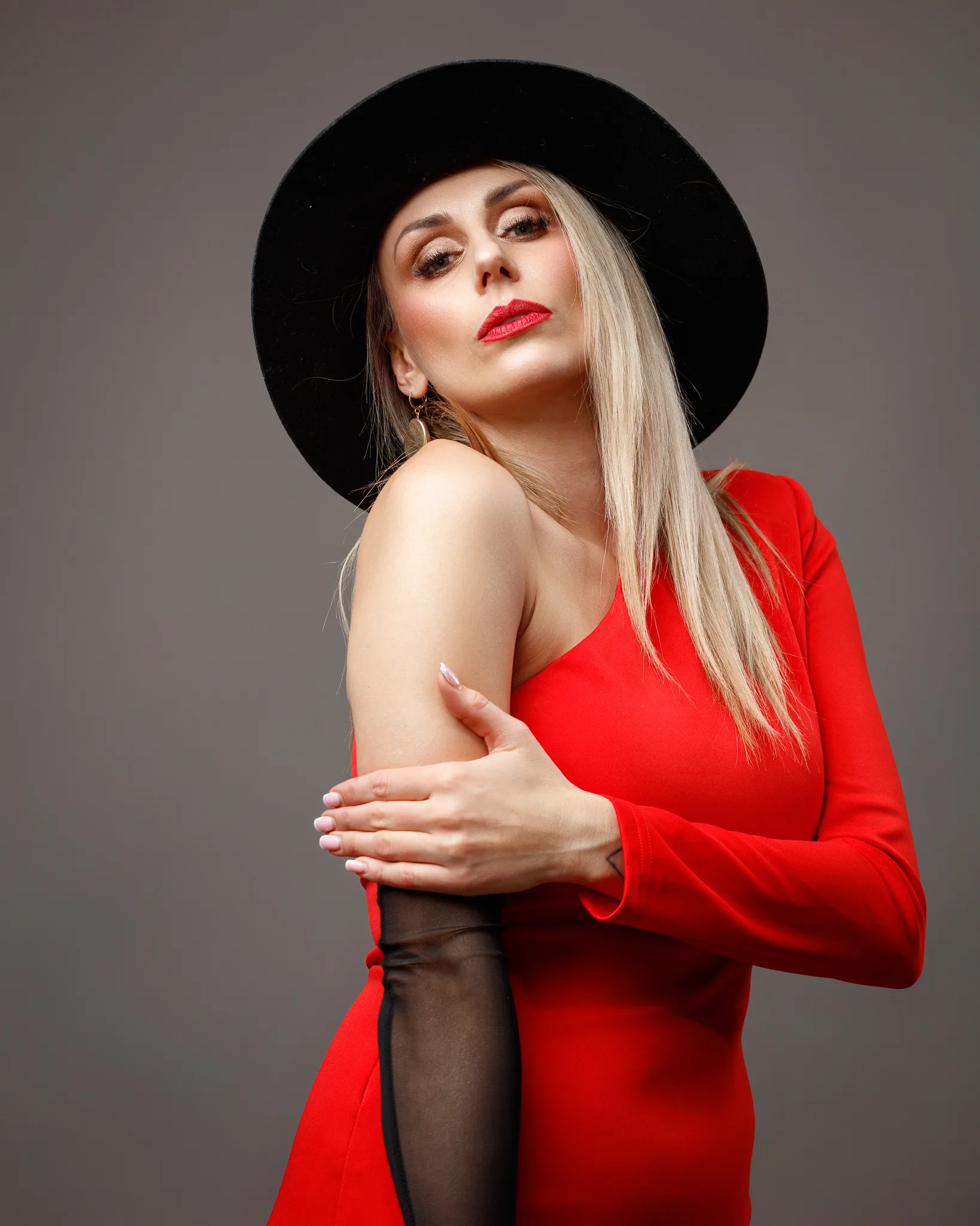 Woman in red dress and black hat posing confidently.