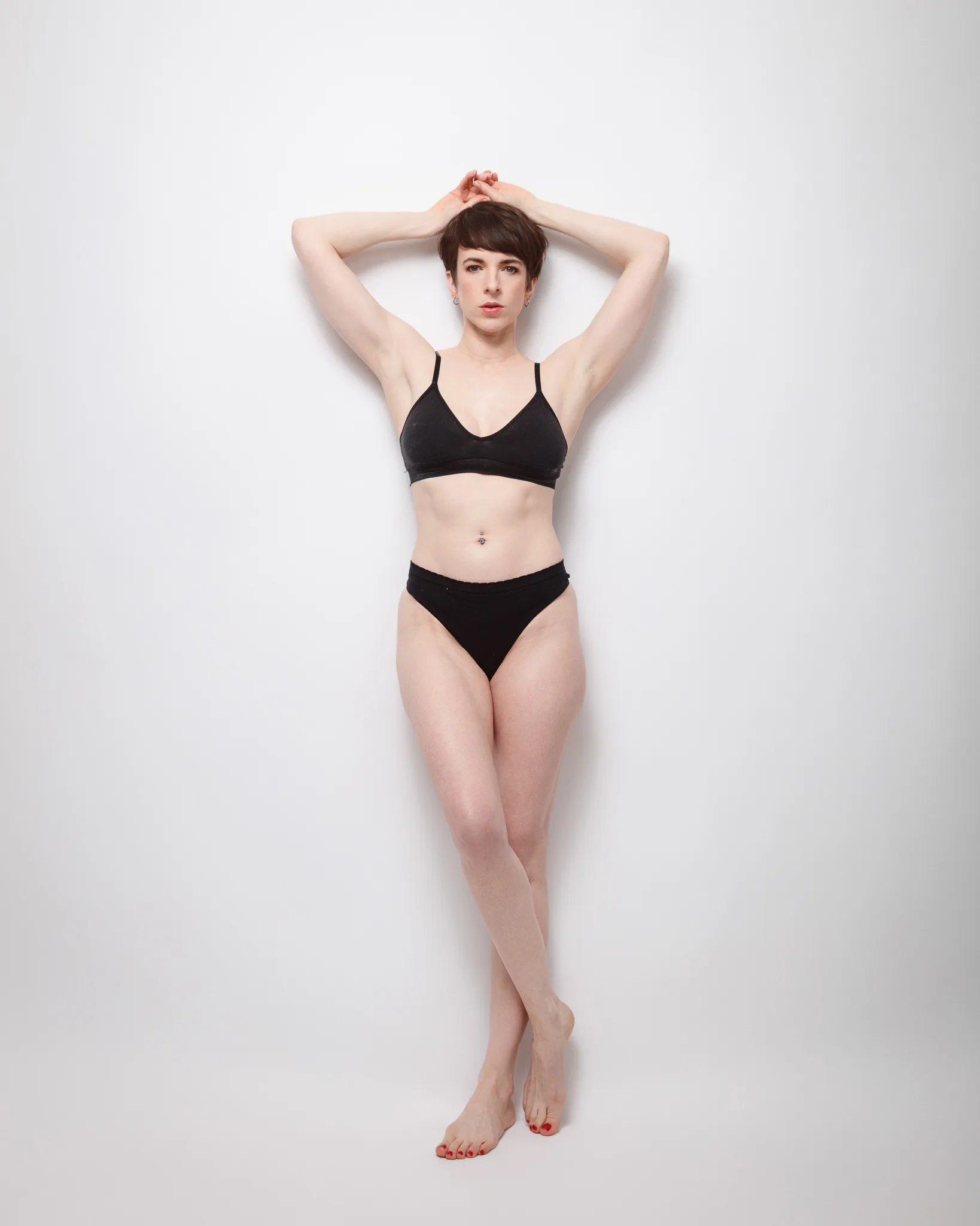 Person posing in black underwear against white background.
