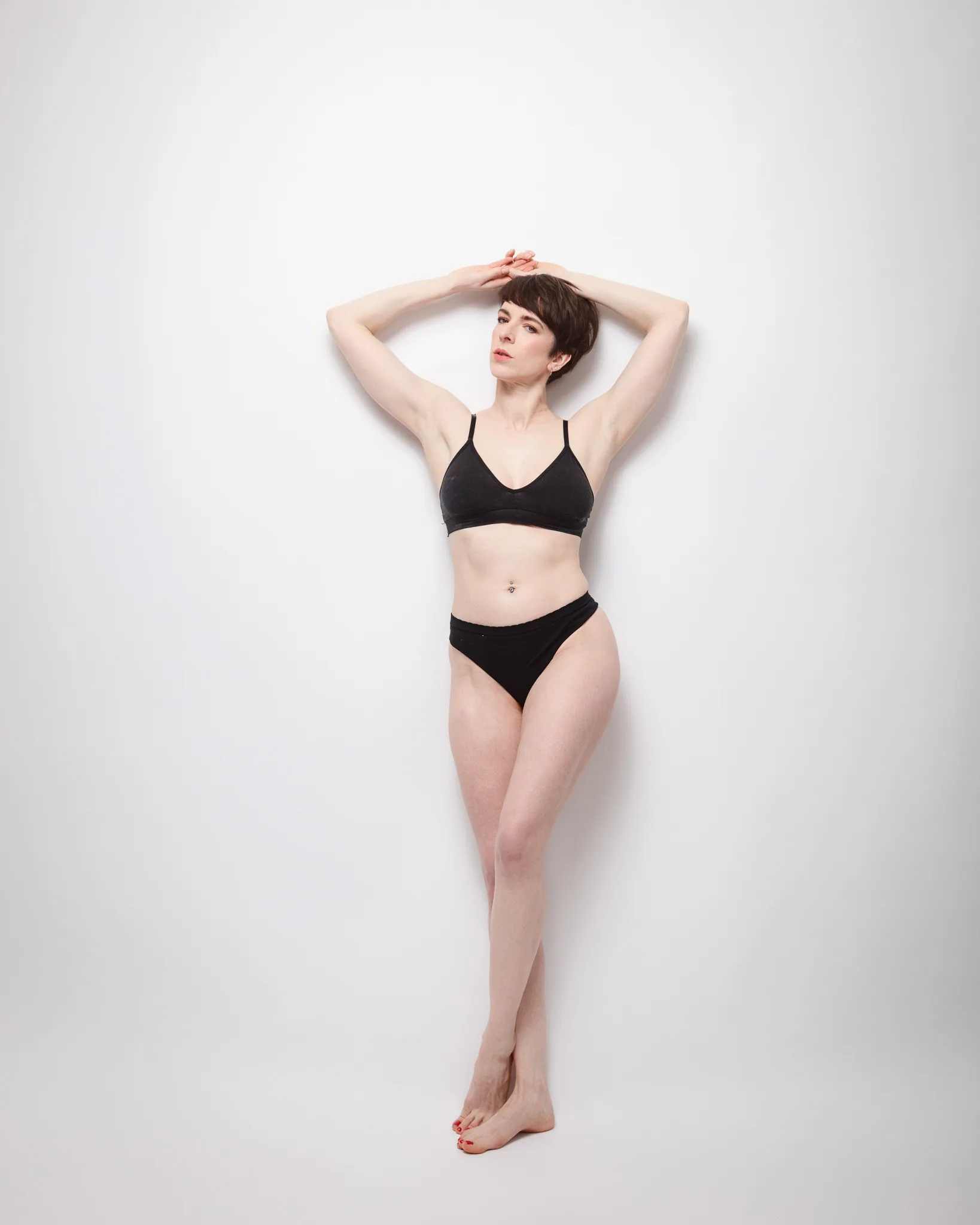 Woman posing in black underwear against white background.