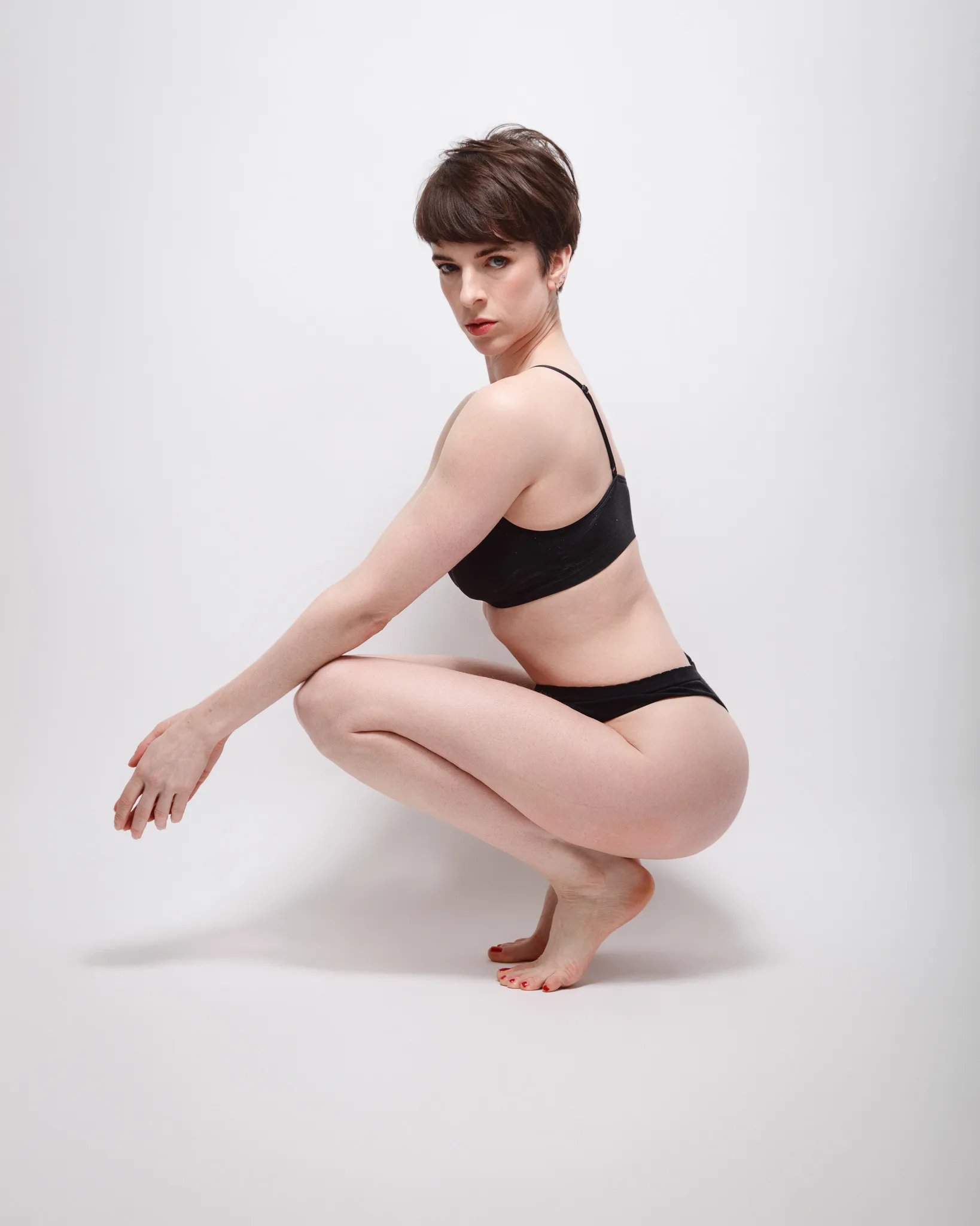Person squatting in black underwear on white background.