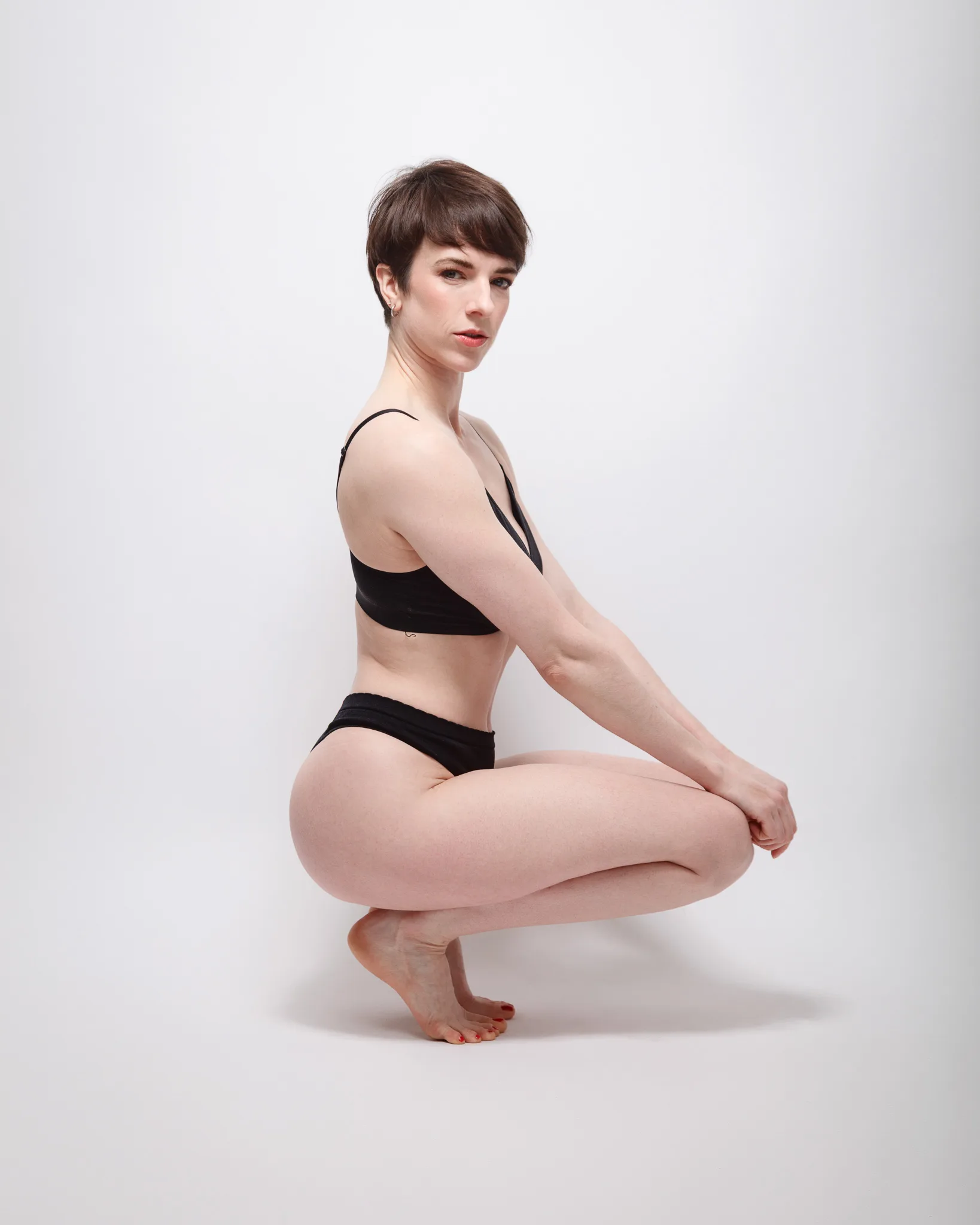 Person crouching in black underwear against white background.
