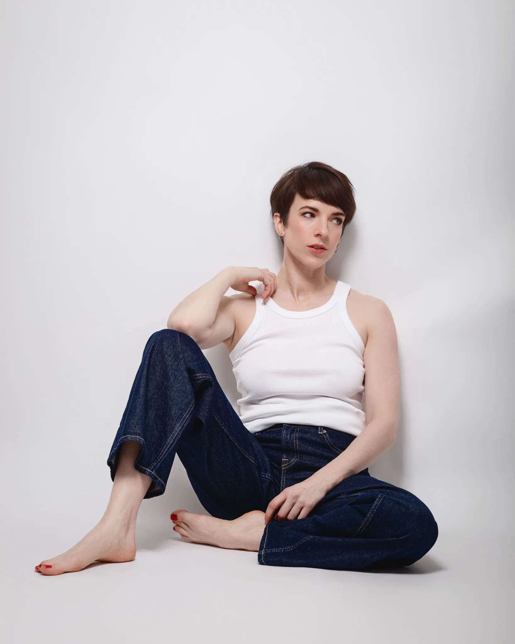 Person in white top and jeans sitting thoughtfully.