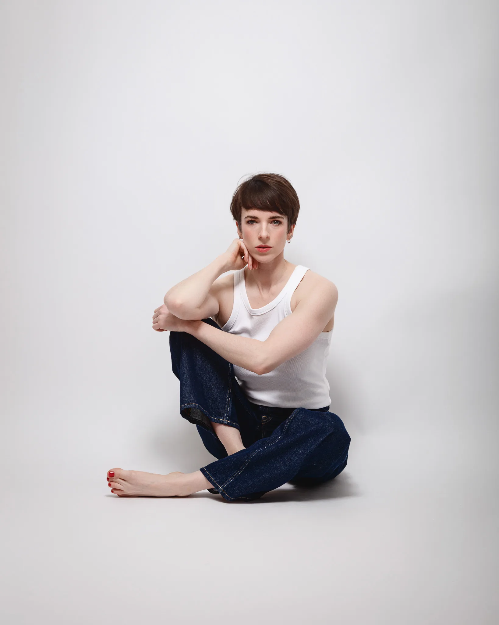 Person seated in white top and jeans, minimalist setting.