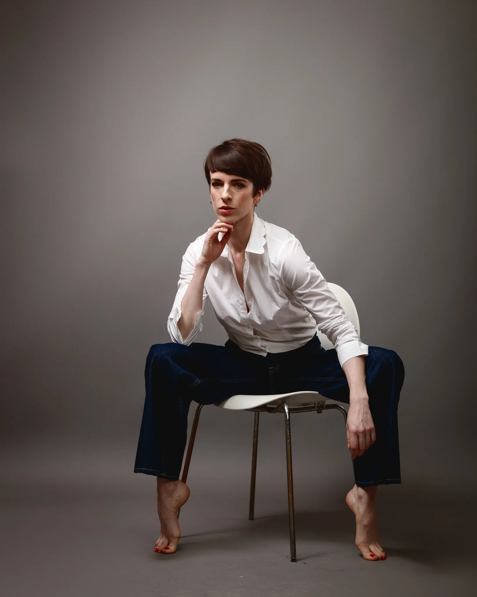 Person seated on chair, wearing white shirt, jeans.