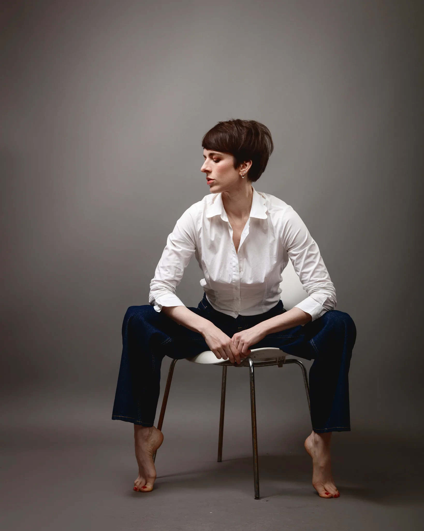 Person sitting on chair, wearing white shirt and jeans.