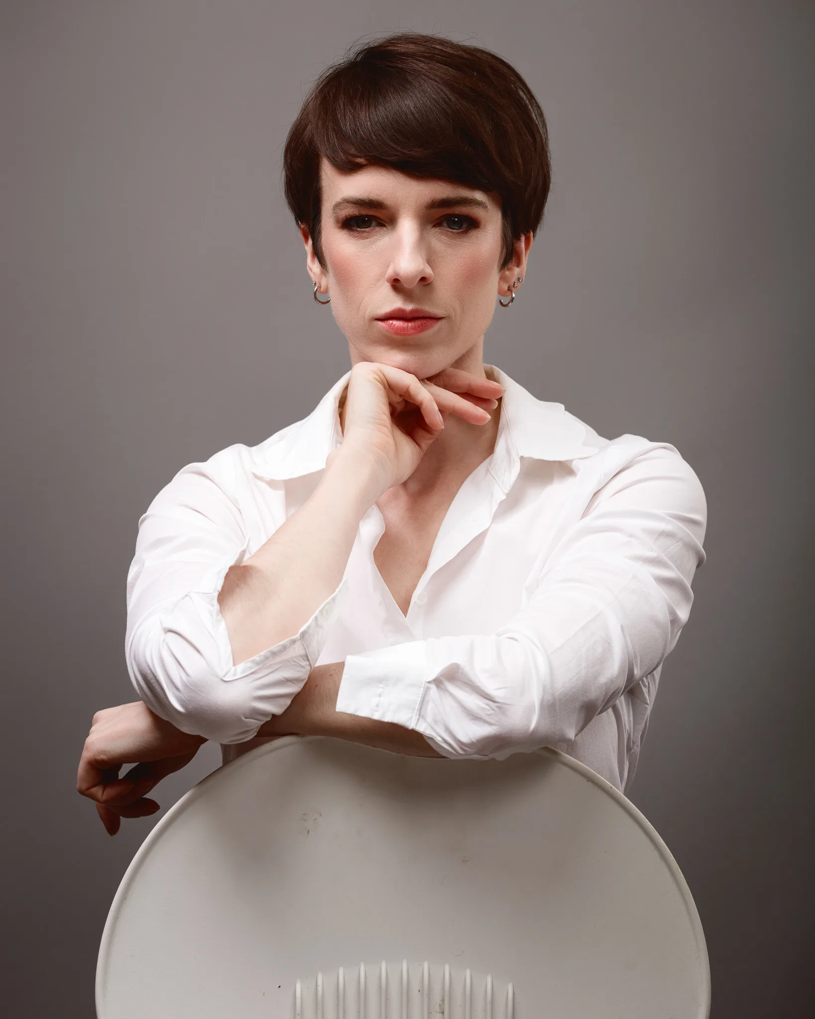 Person in white shirt seated behind chair, thoughtful pose.