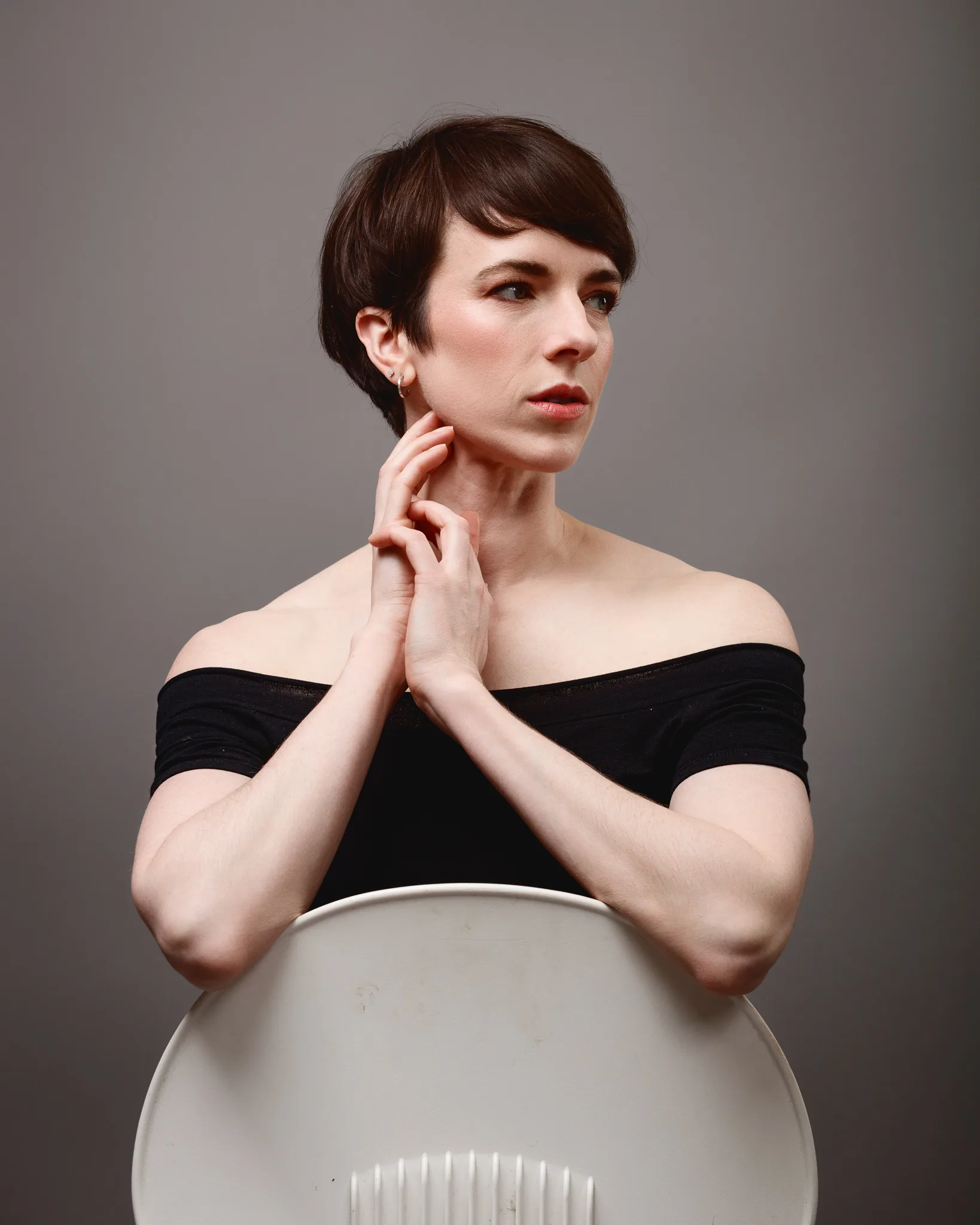 Woman in black top, seated behind chair.