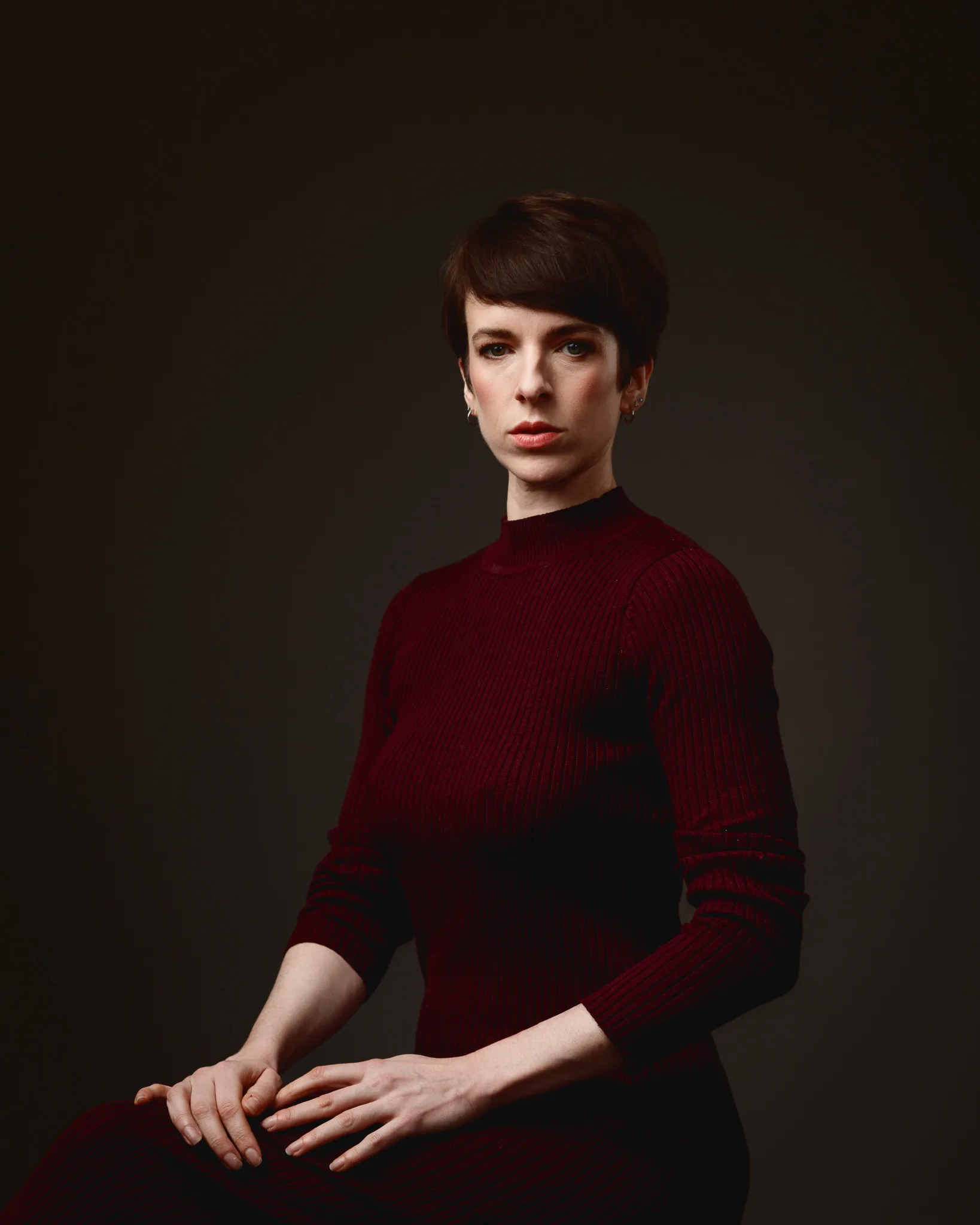 Person in maroon sweater against dark background.