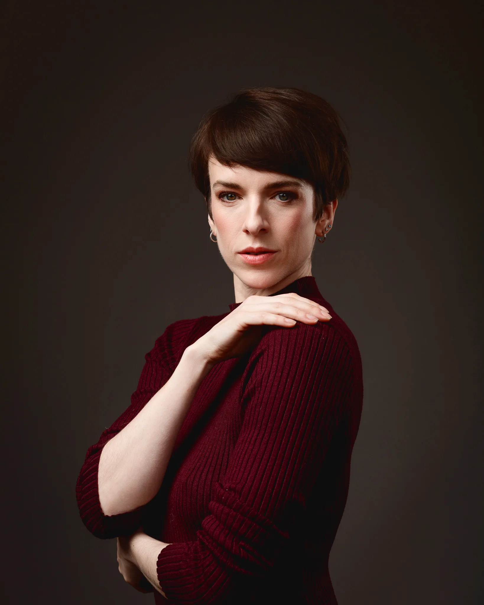 Person in burgundy sweater posing stylishly against dark background.