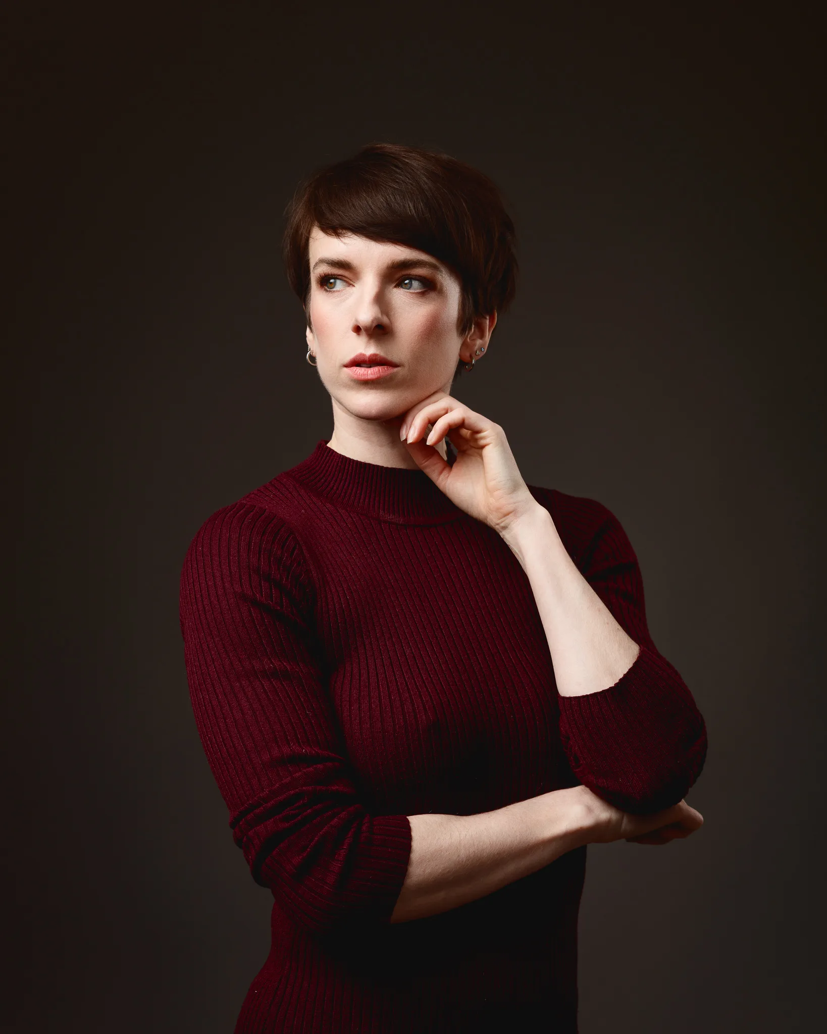 Thoughtful person in a red jumper on dark background.