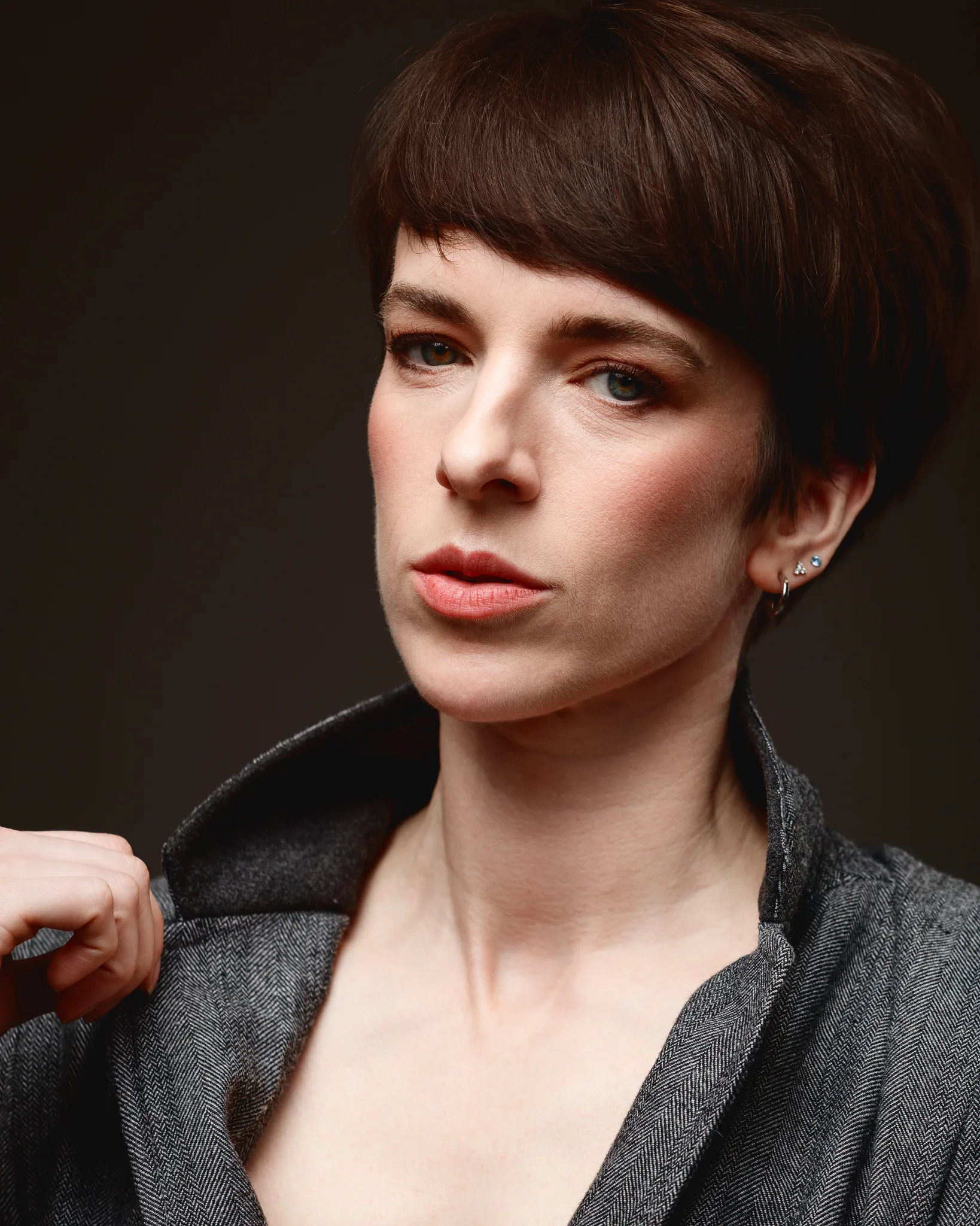 Person with short hair, adjusting collar, serious expression.