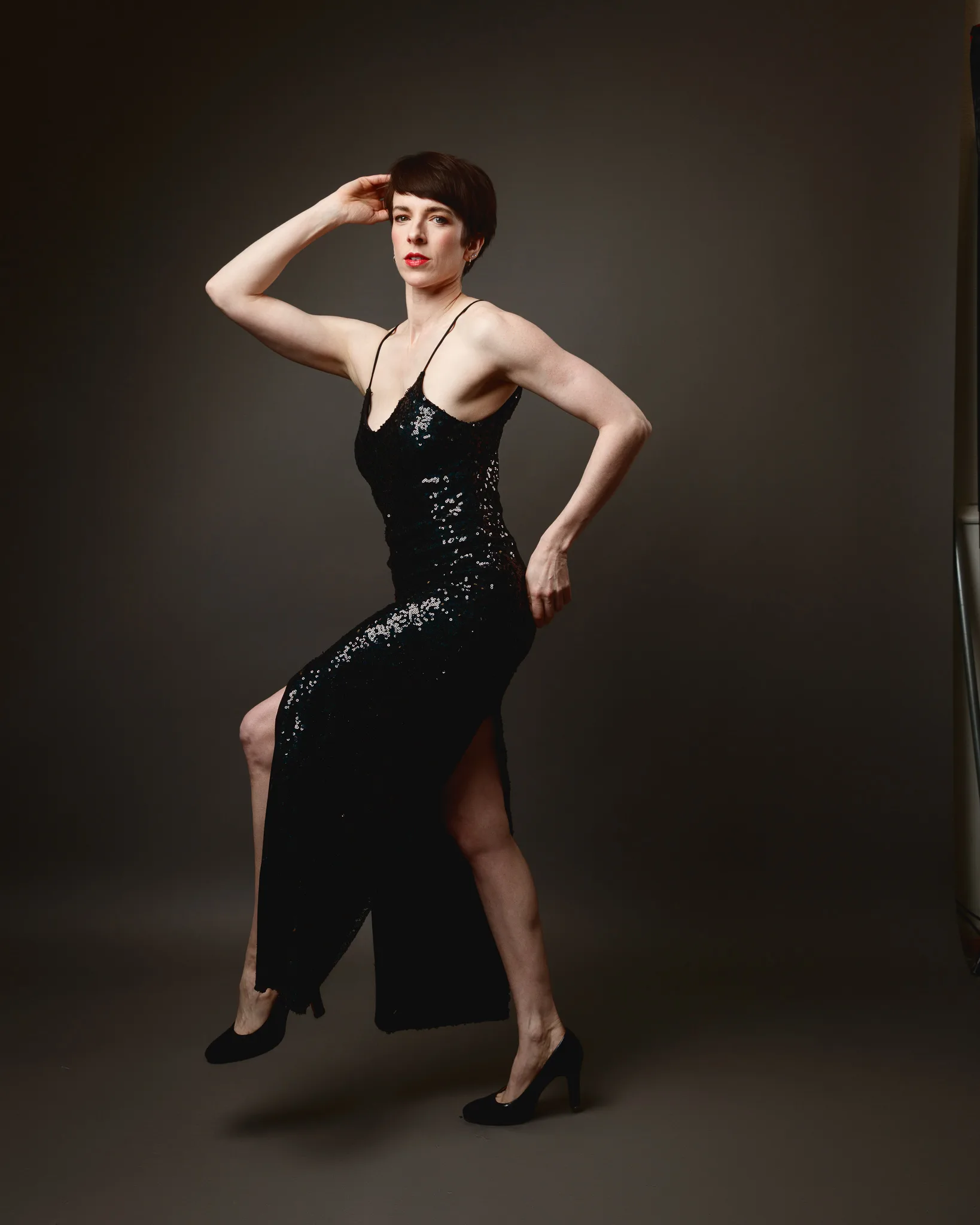 Person posing in elegant black dress, dramatic lighting.