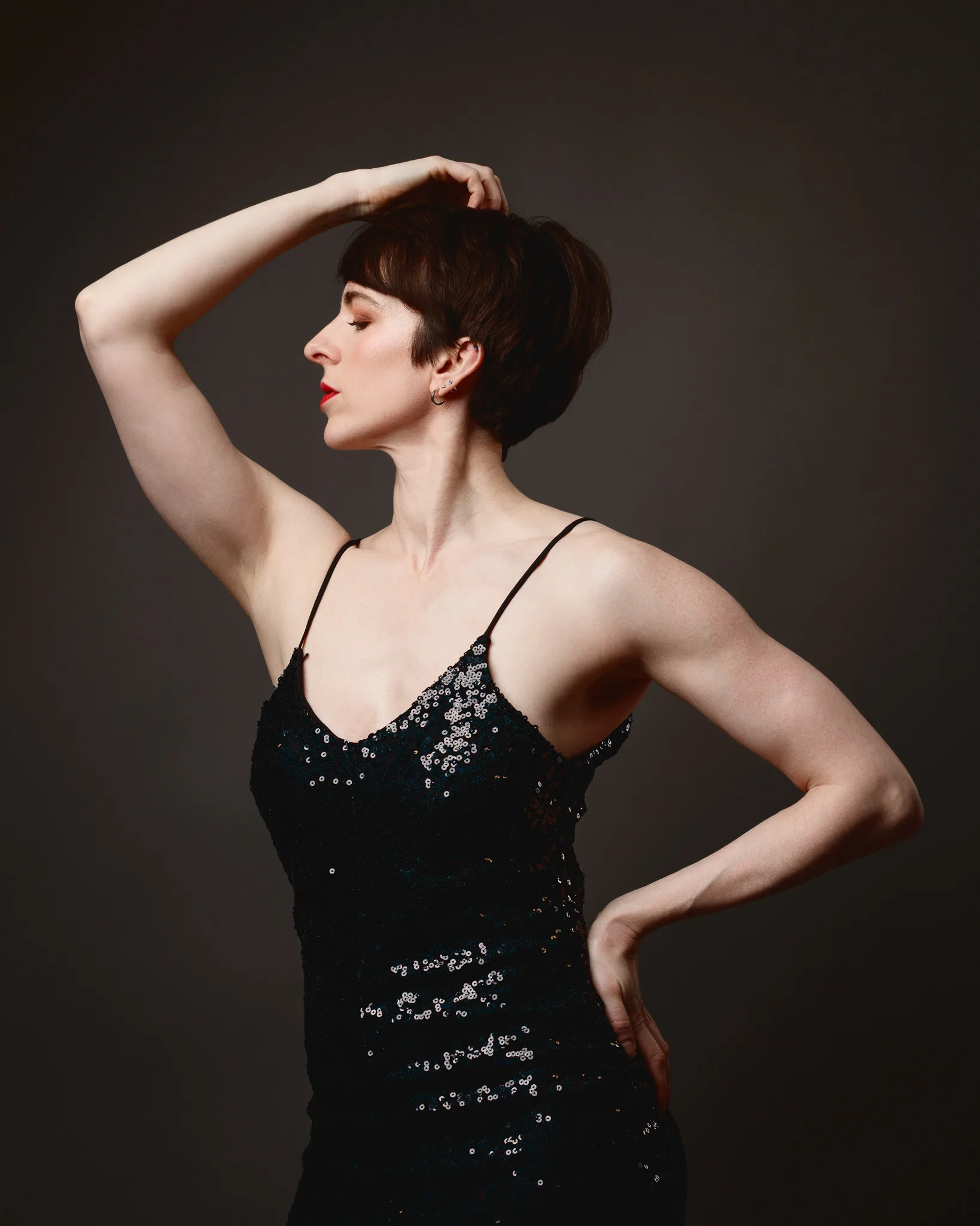 Person posing in black sequin dress, dramatic lighting.