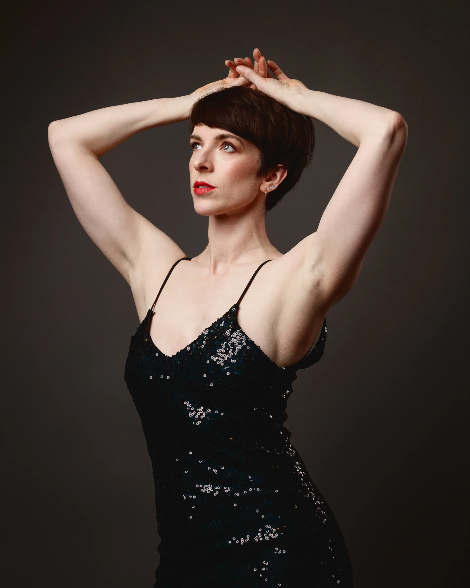 Woman in sequin dress posing with raised arms.