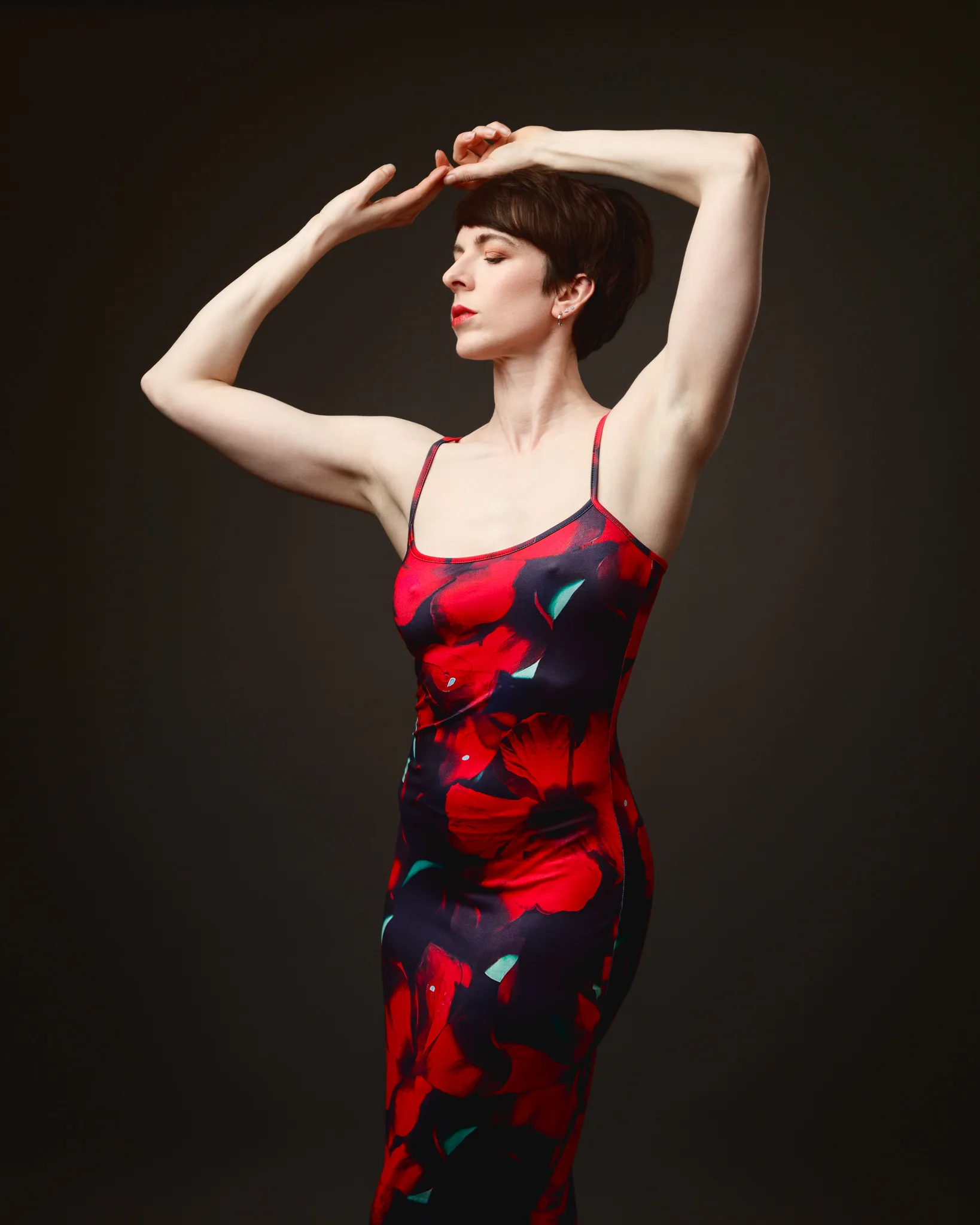 Woman in floral dress posing elegantly against dark background.