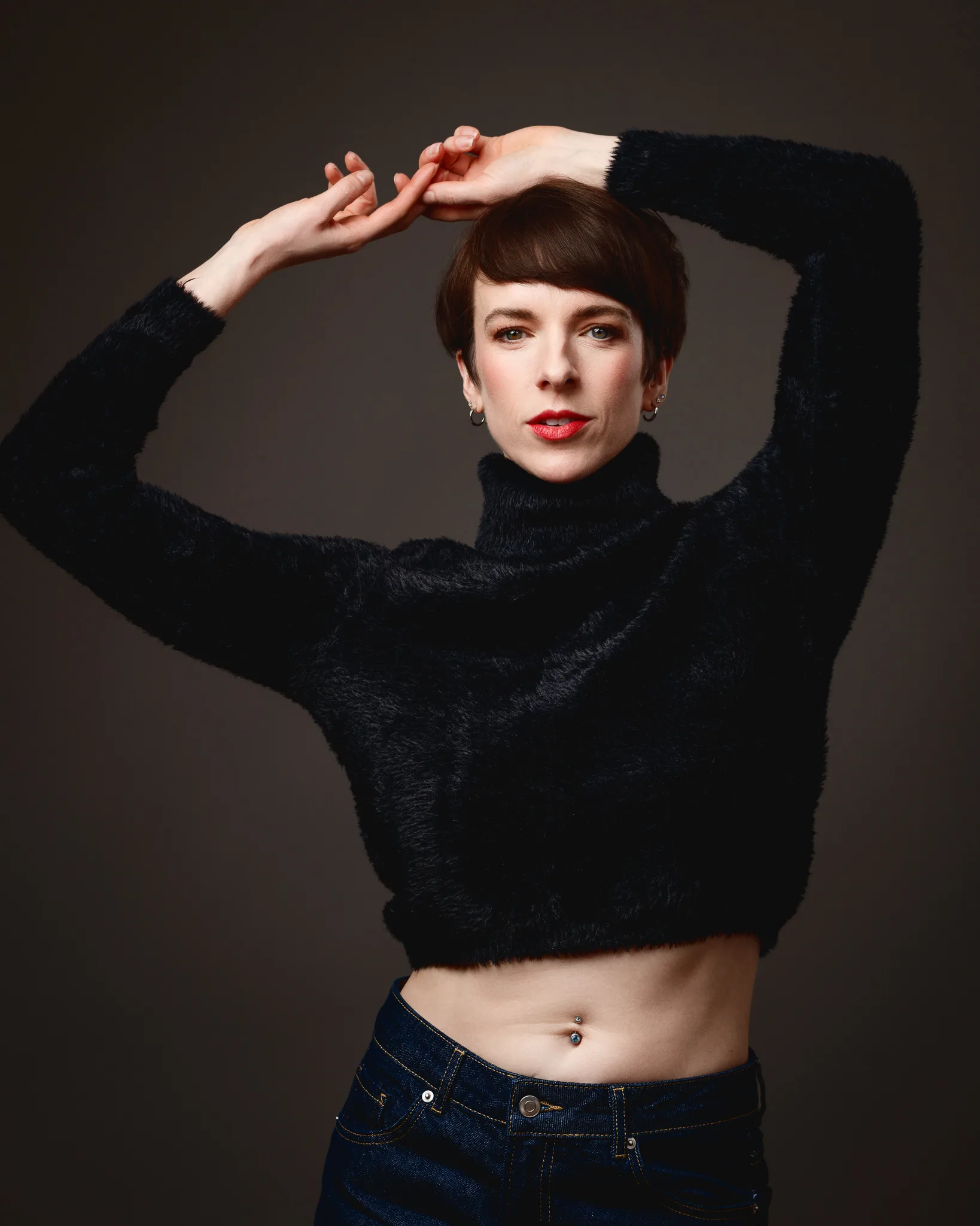 Person posing with arms raised in dark outfit.