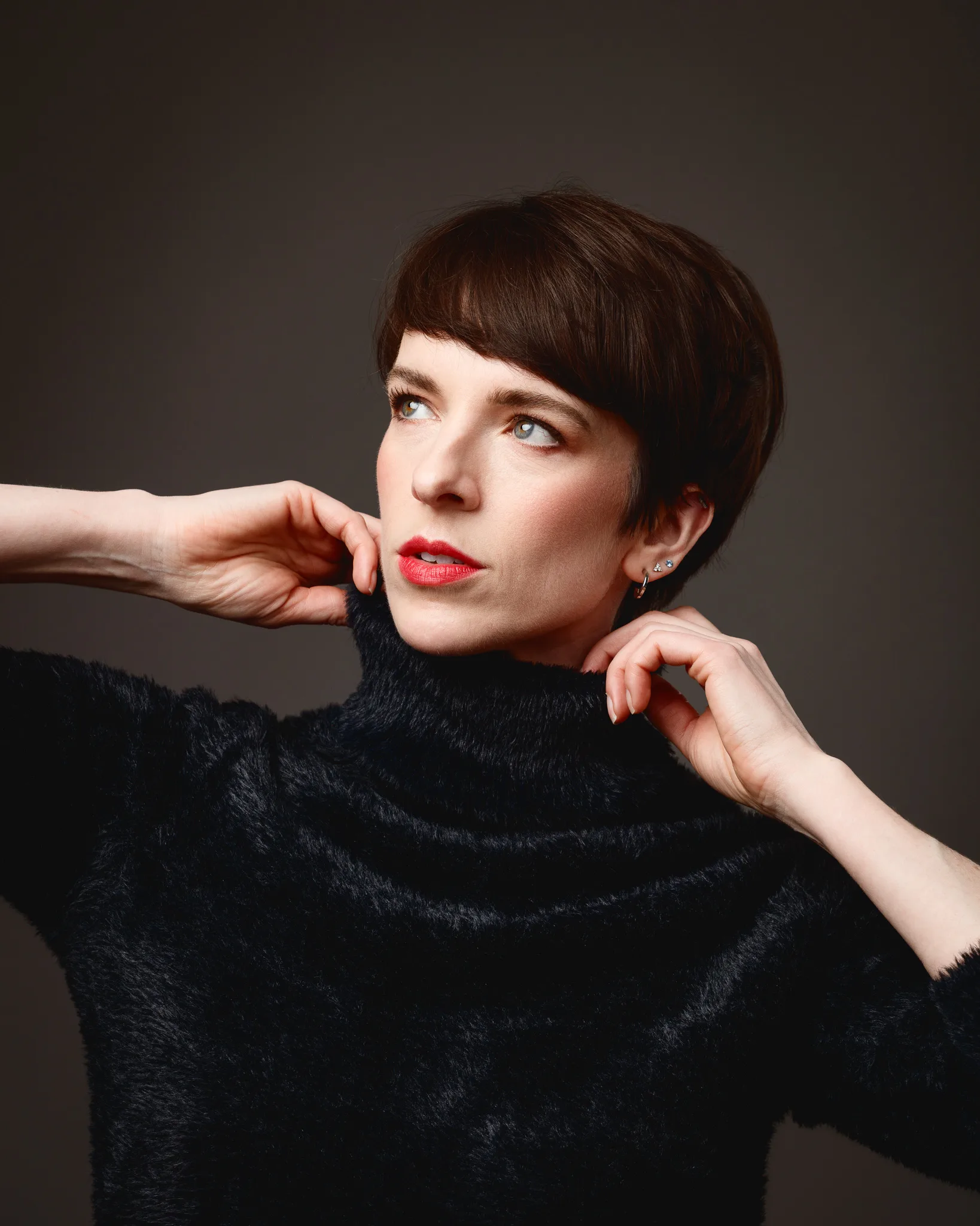Person adjusting black turtleneck in studio portrait.