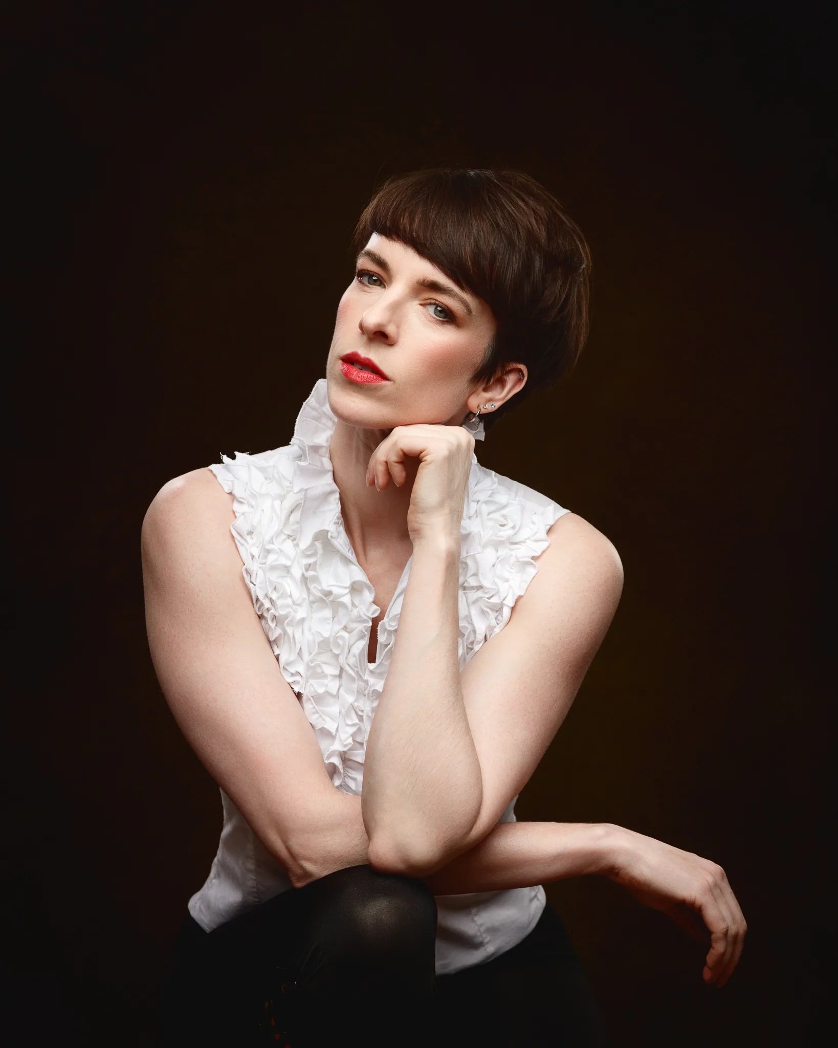 Person in white ruffled blouse, dark background.