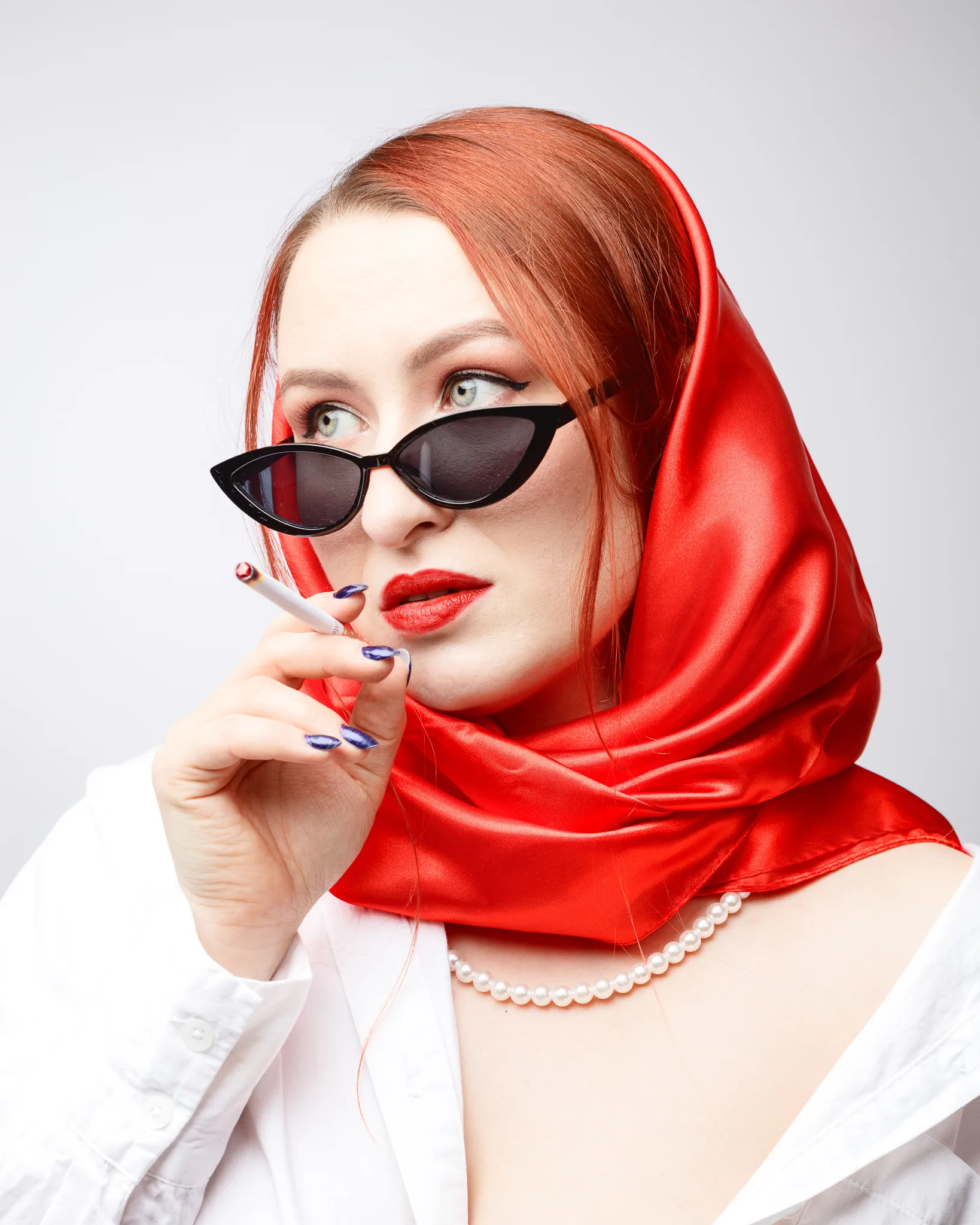 Woman in red scarf, sunglasses holding cigarette.