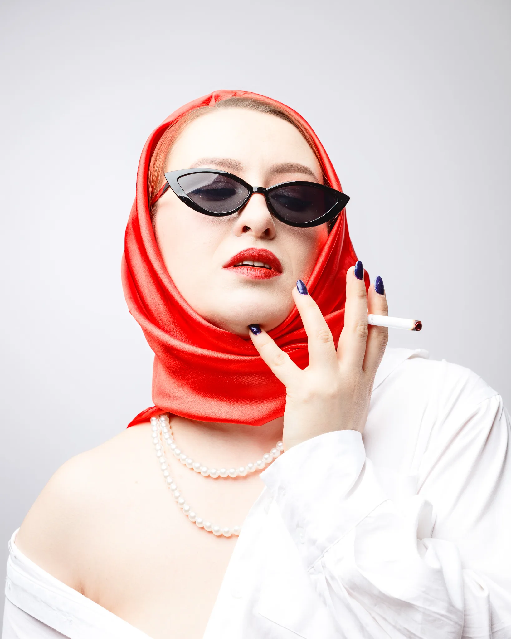 Woman in red scarf, sunglasses, holding cigarette.