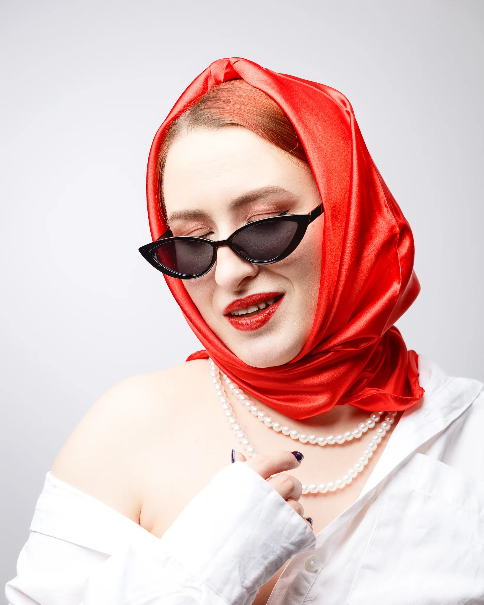 Woman in red headscarf with sunglasses and pearls.
