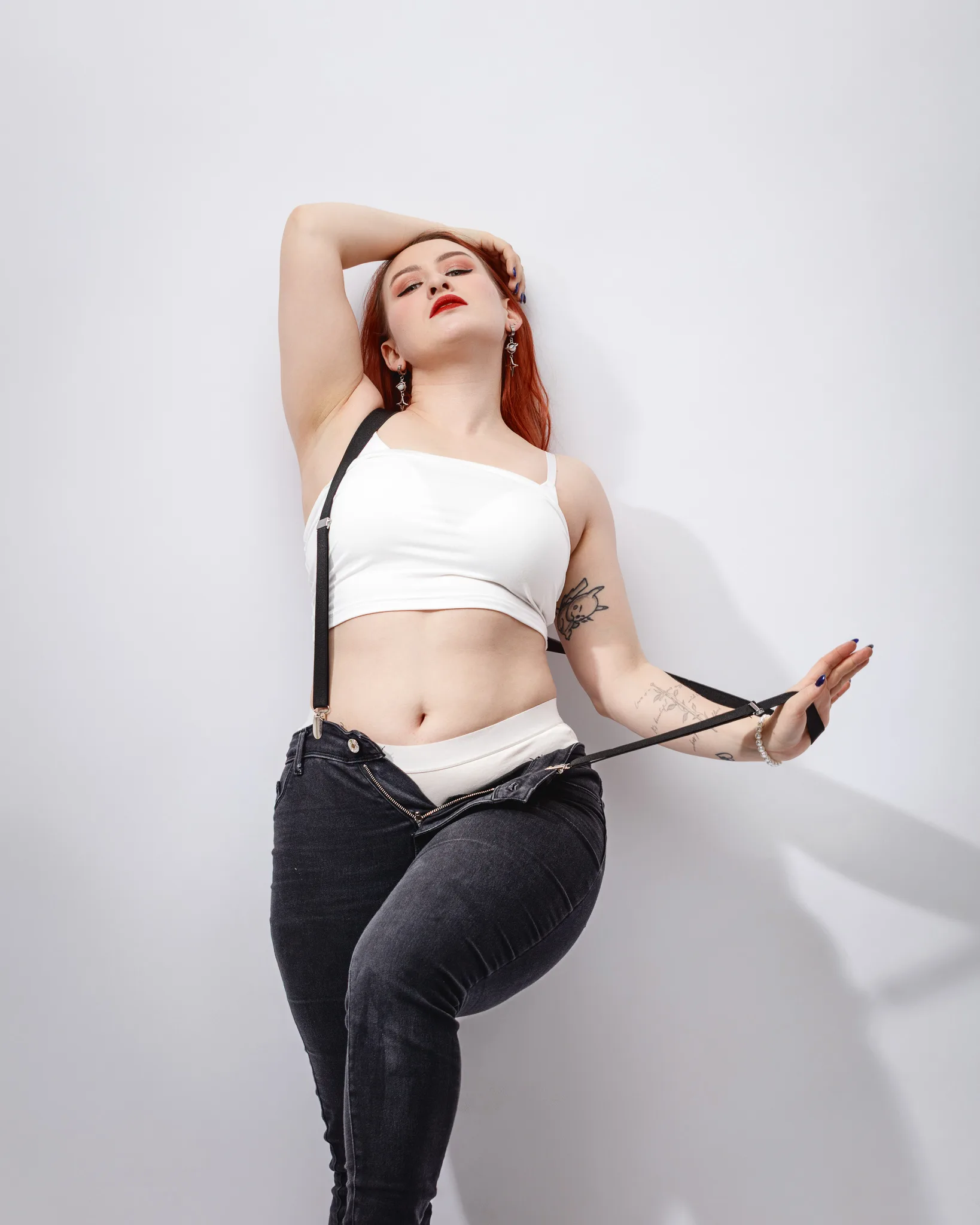 Confident person posing with tattoo and suspenders.