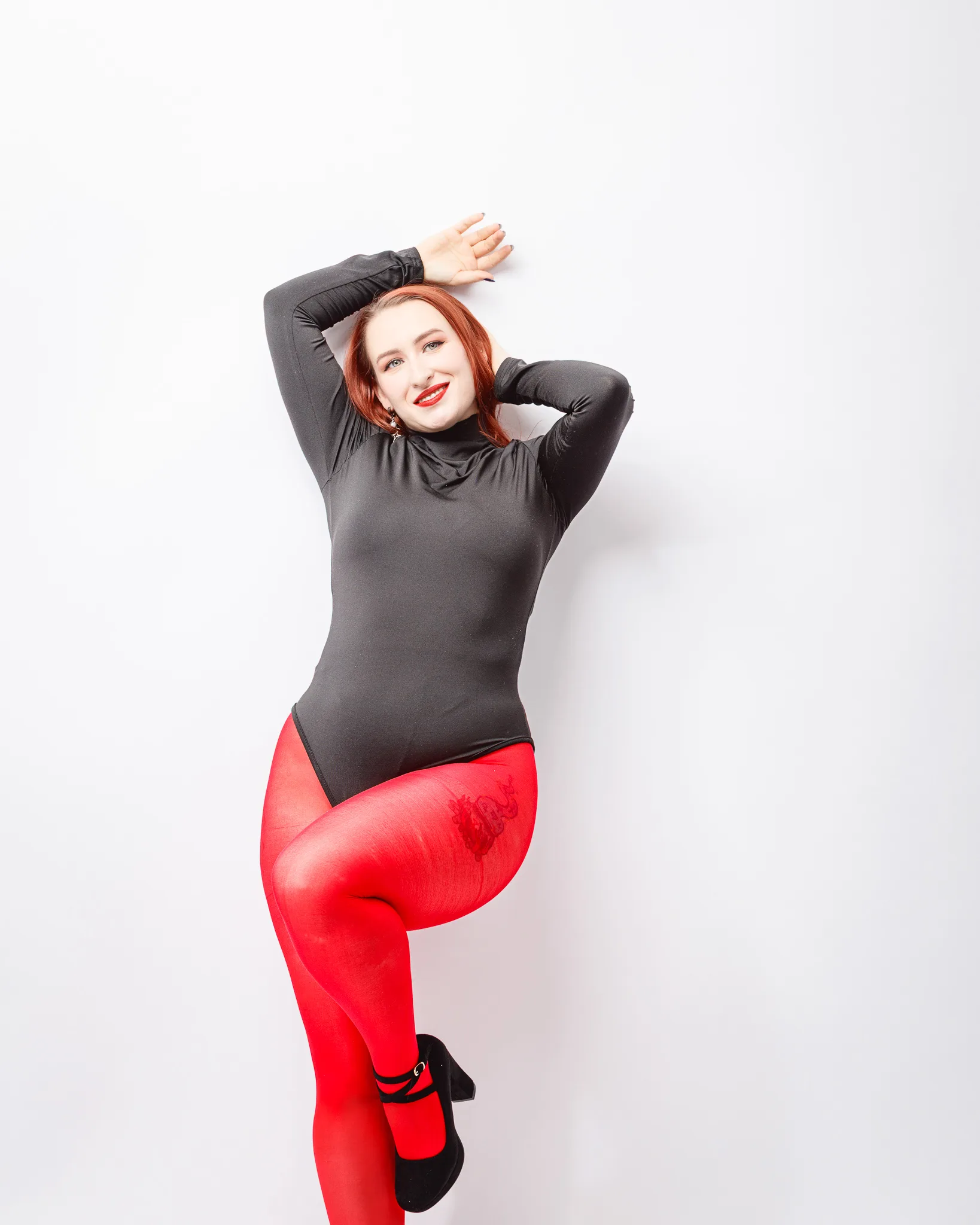 Woman posing in black bodysuit and red tights.