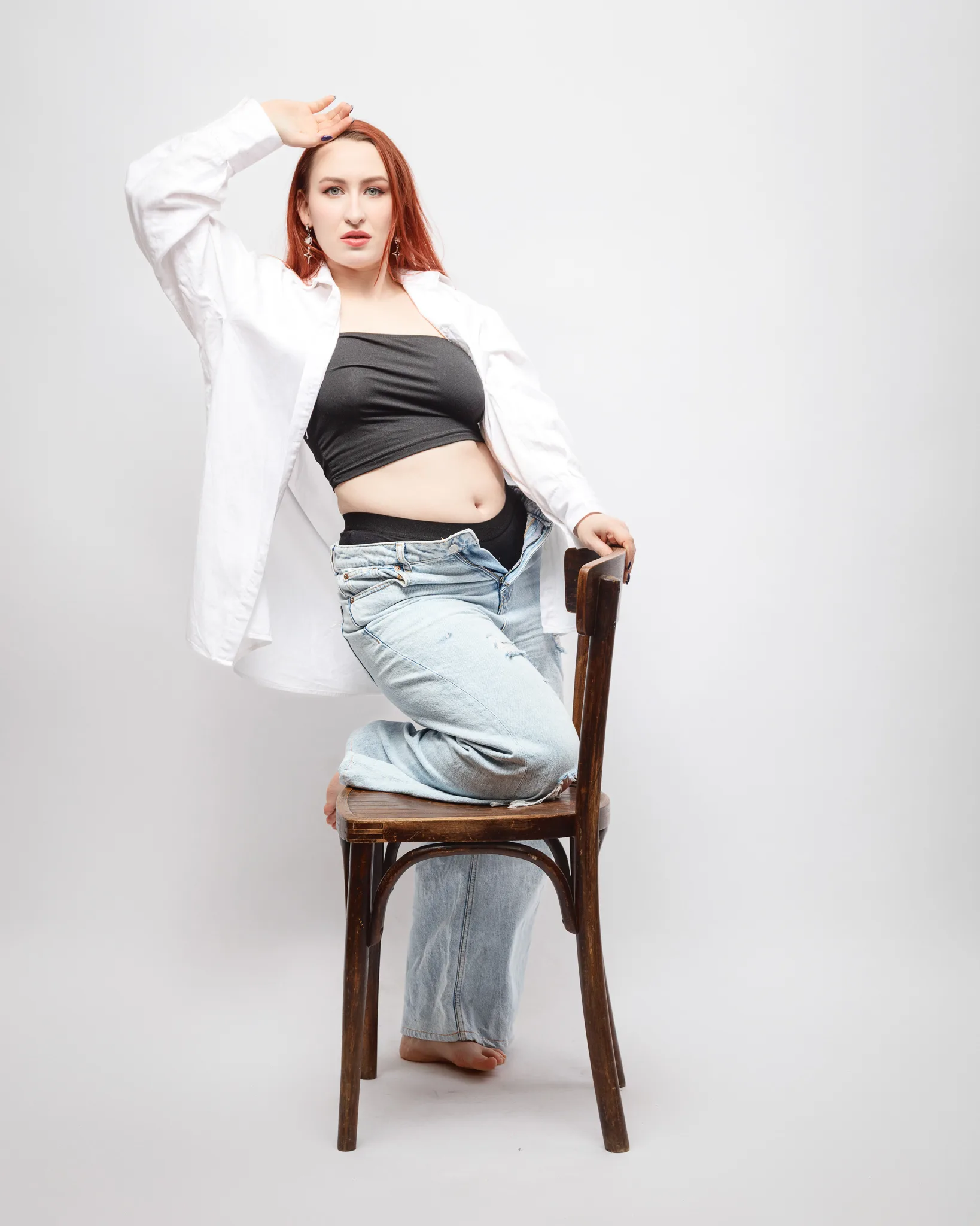 Person posing on chair, wearing casual jeans and shirt.