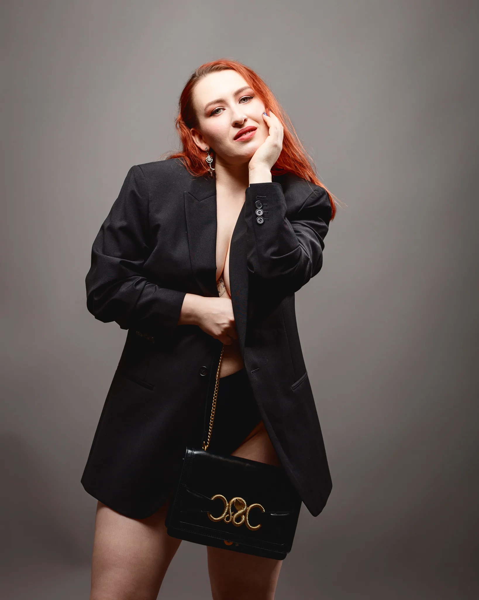Woman in blazer holding black handbag, posing confidently.